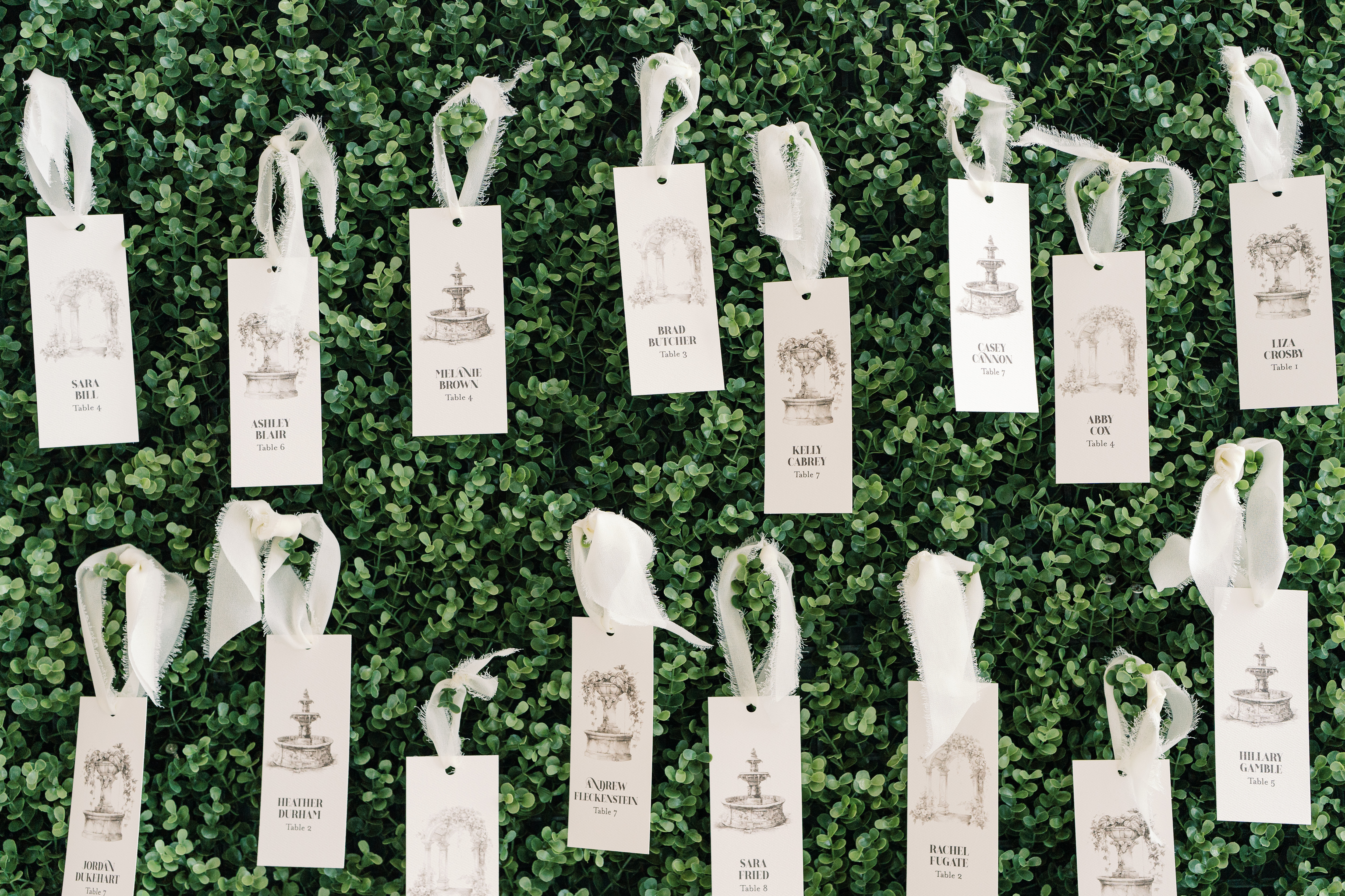 Escort cards displayed on hedge wall.