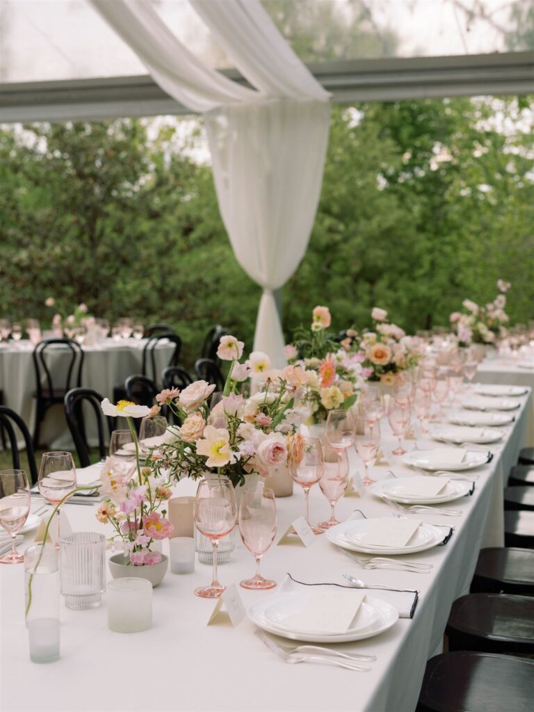 Outdoor reception tent and tables with tablescapes and floral decor.