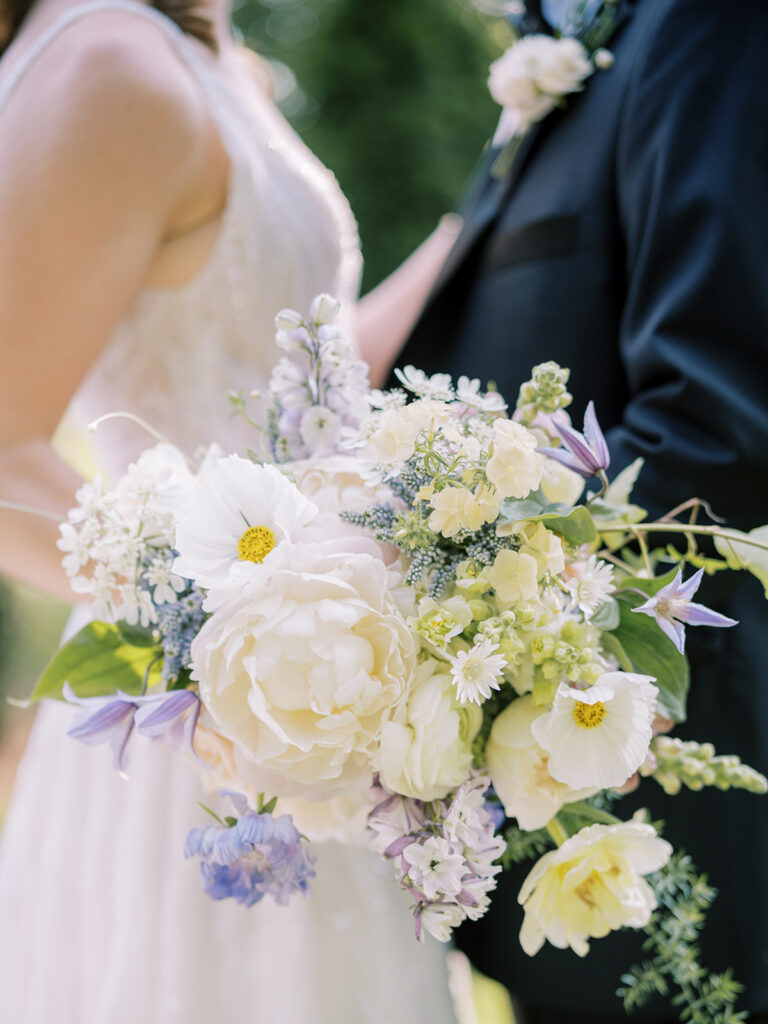 Wedding bouquet in focus with bride and groom in the background.