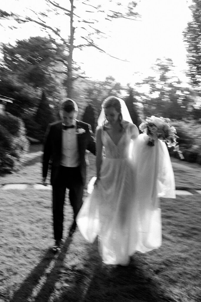 black and white image of bride and groom walking together along outside path.