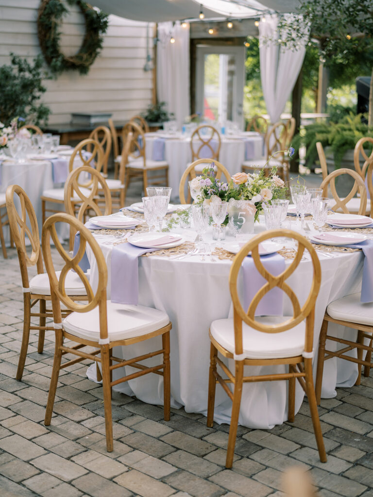 Formal reception setting with tables, chairs on cobblestone floor showing place setting, florals and table signage.