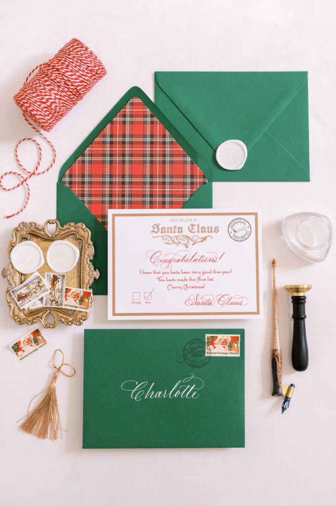 Plaid-lined green envelope displaying a Letter from Santa. Styled with tray of white wax seals, seal press, calligraphy pen, string and tassel.