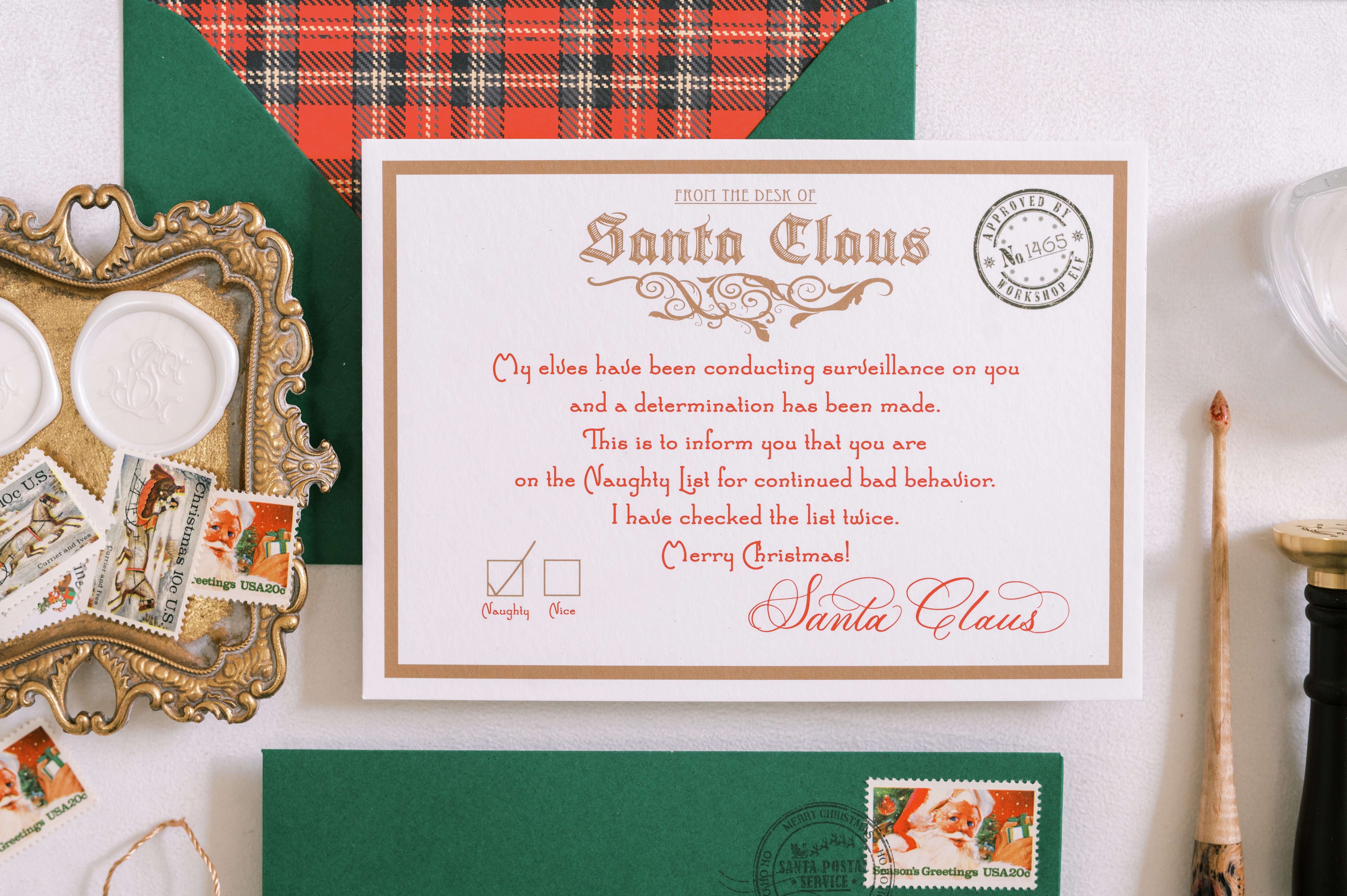 Plaid-lined green envelope displaying a Letter from Santa. Styled with tray of white wax seals, seal press, calligraphy pen, string and tassel.