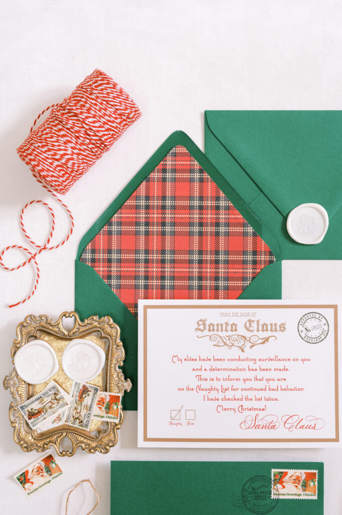 Plaid-lined green envelope displaying a Letter from Santa. Styled with tray of white wax seals, seal press, calligraphy pen, string and tassel.