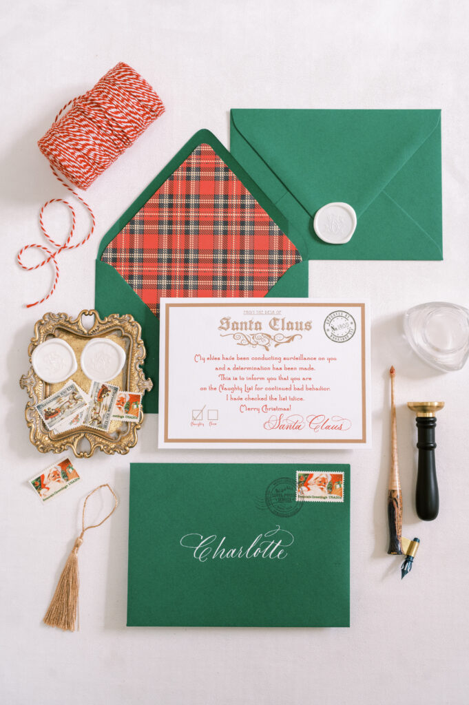 Plaid-lined green envelope displaying a Letter from Santa. Styled with tray of white wax seals, seal press, calligraphy pen, string and tassel.
