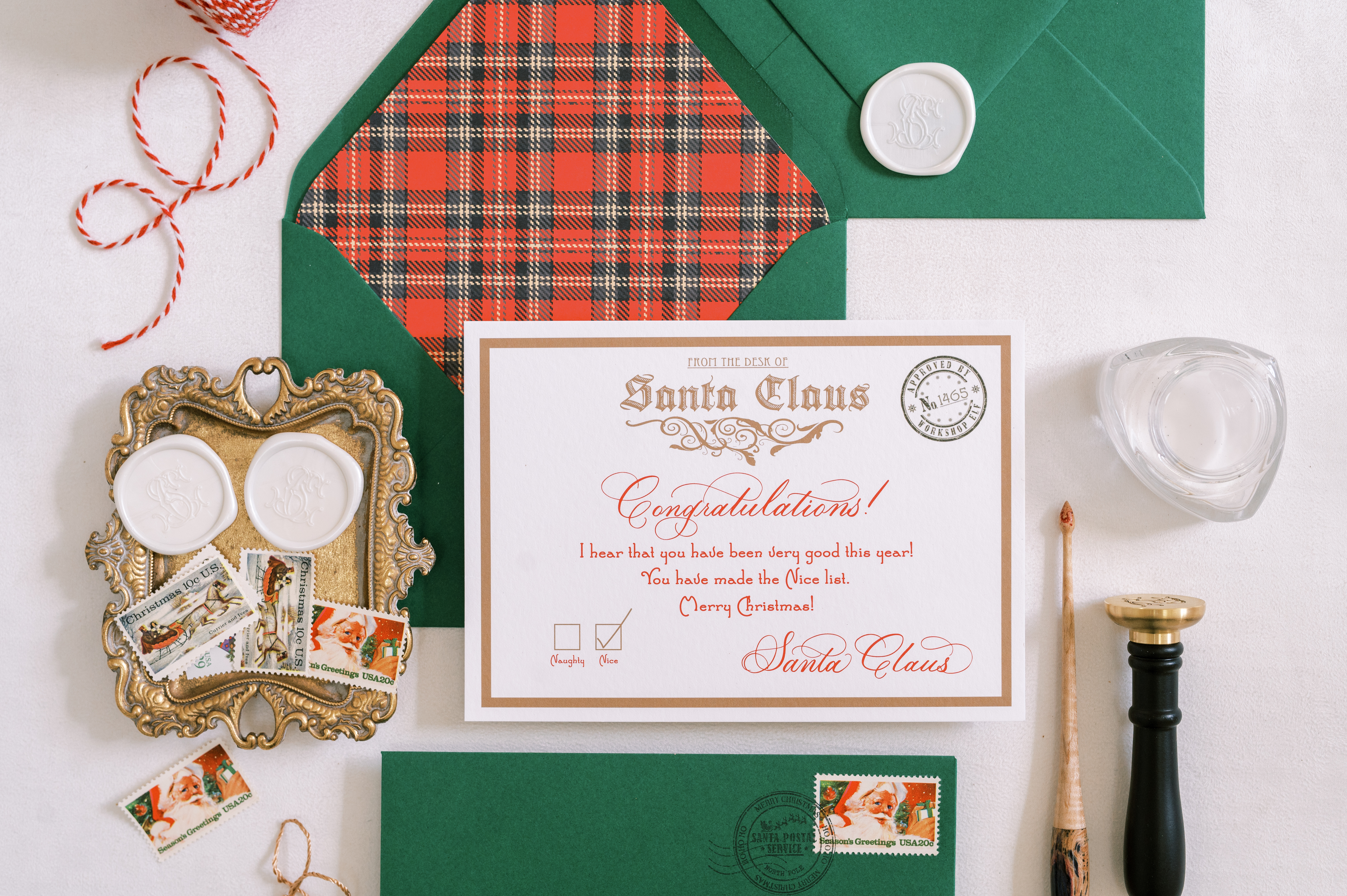 Plaid-lined green envelope displaying a Letter from Santa. Styled with tray of white wax seals, seal press, calligraphy pen, string and tassel.