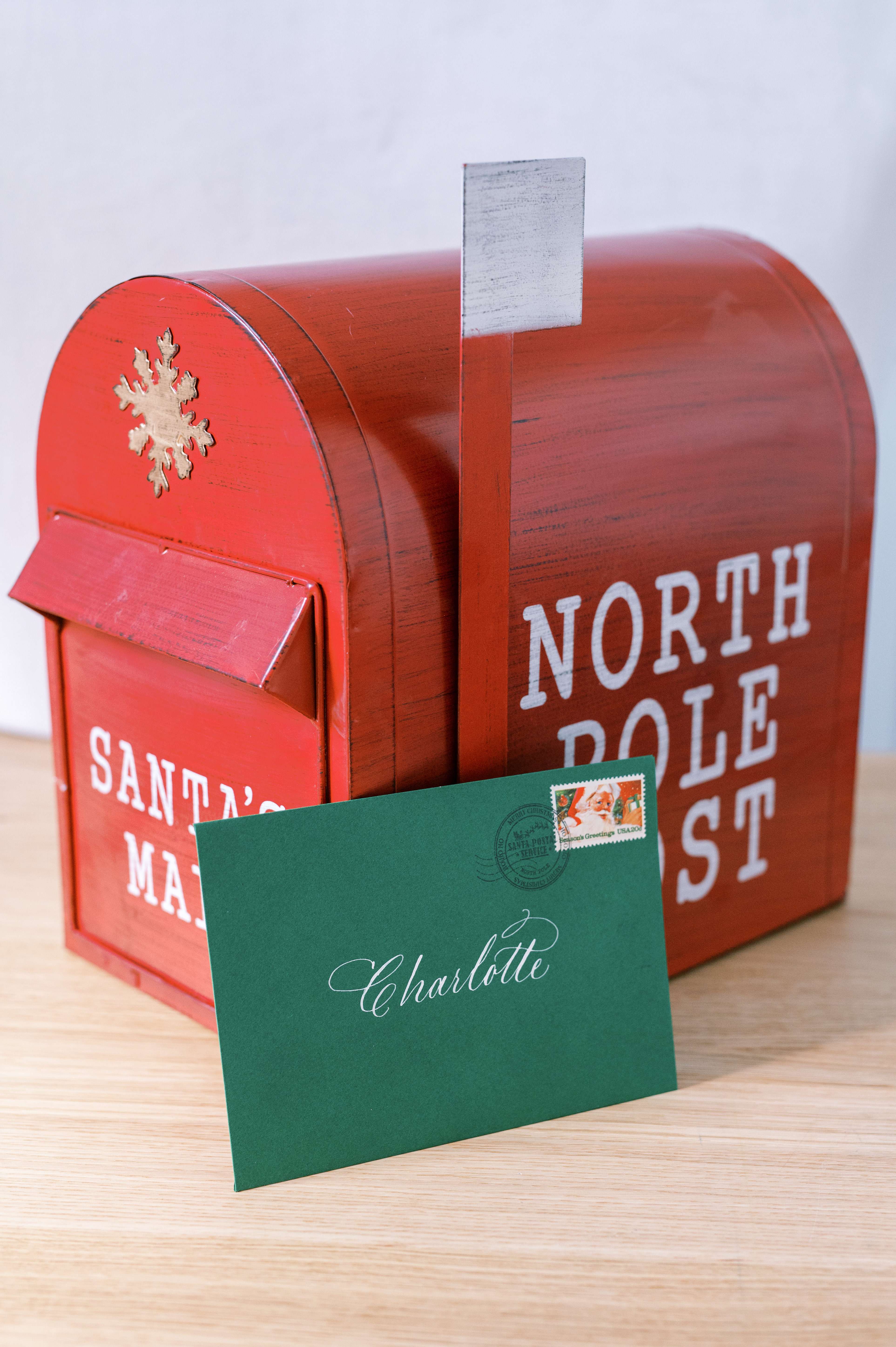 Green envelope with calligraphy and vintage holiday postage inside red mailbox