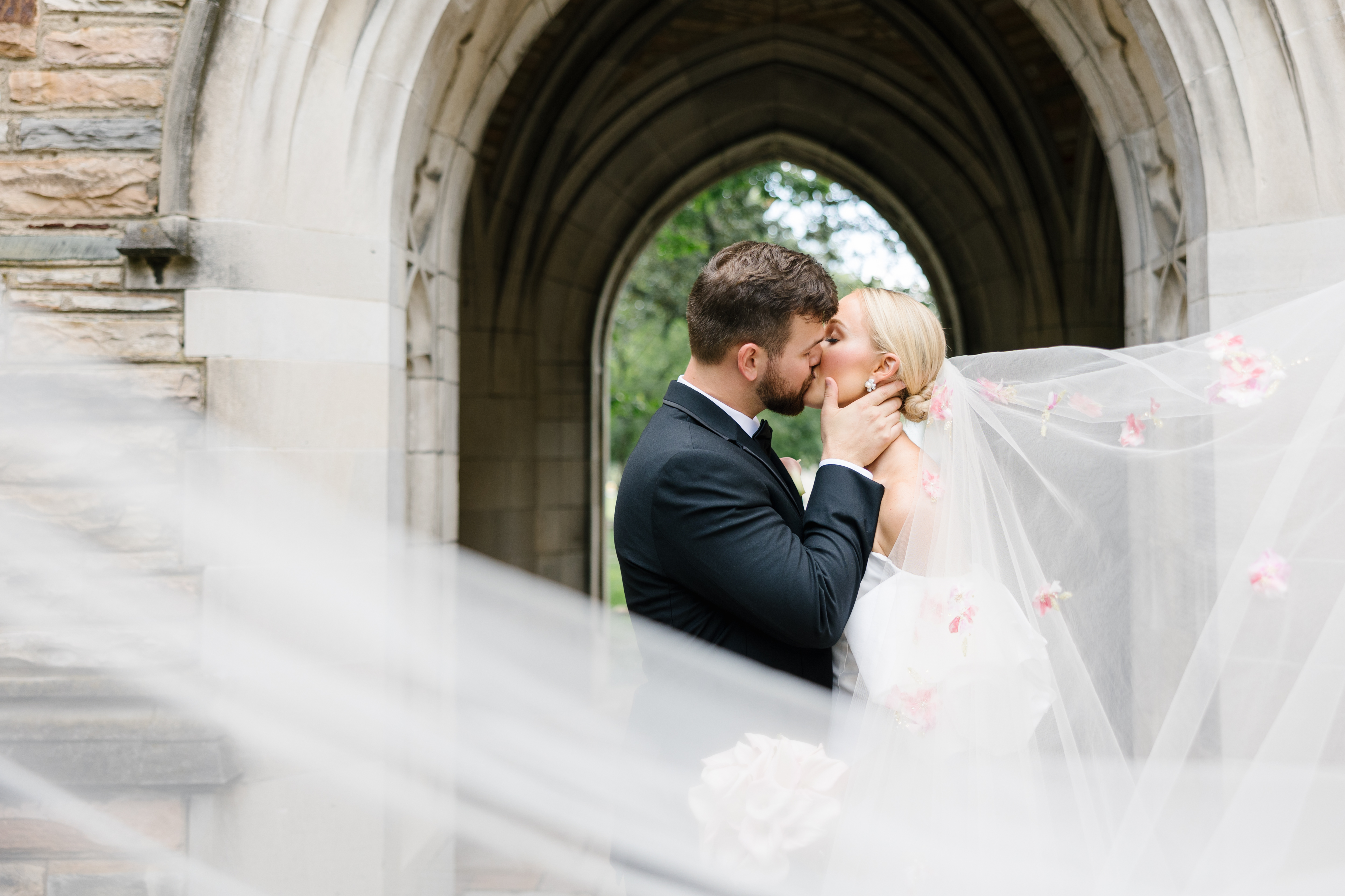 Bride and groom under arch way tunnel. Groom holding bride's face as they share a kiss.