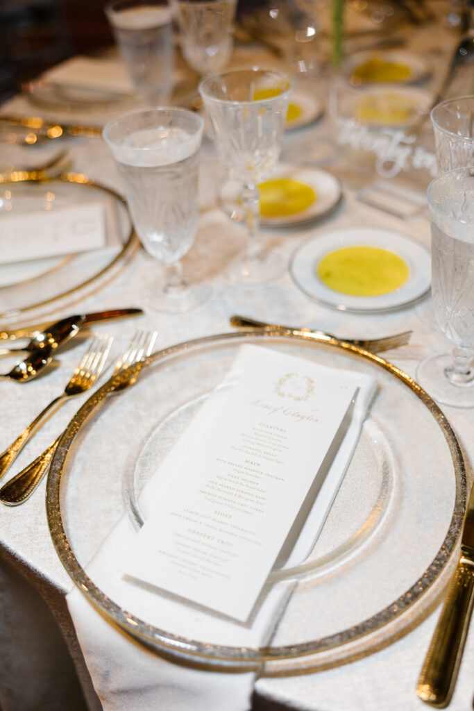 Full place setting including custom dinner menu on top of gold rim plate.