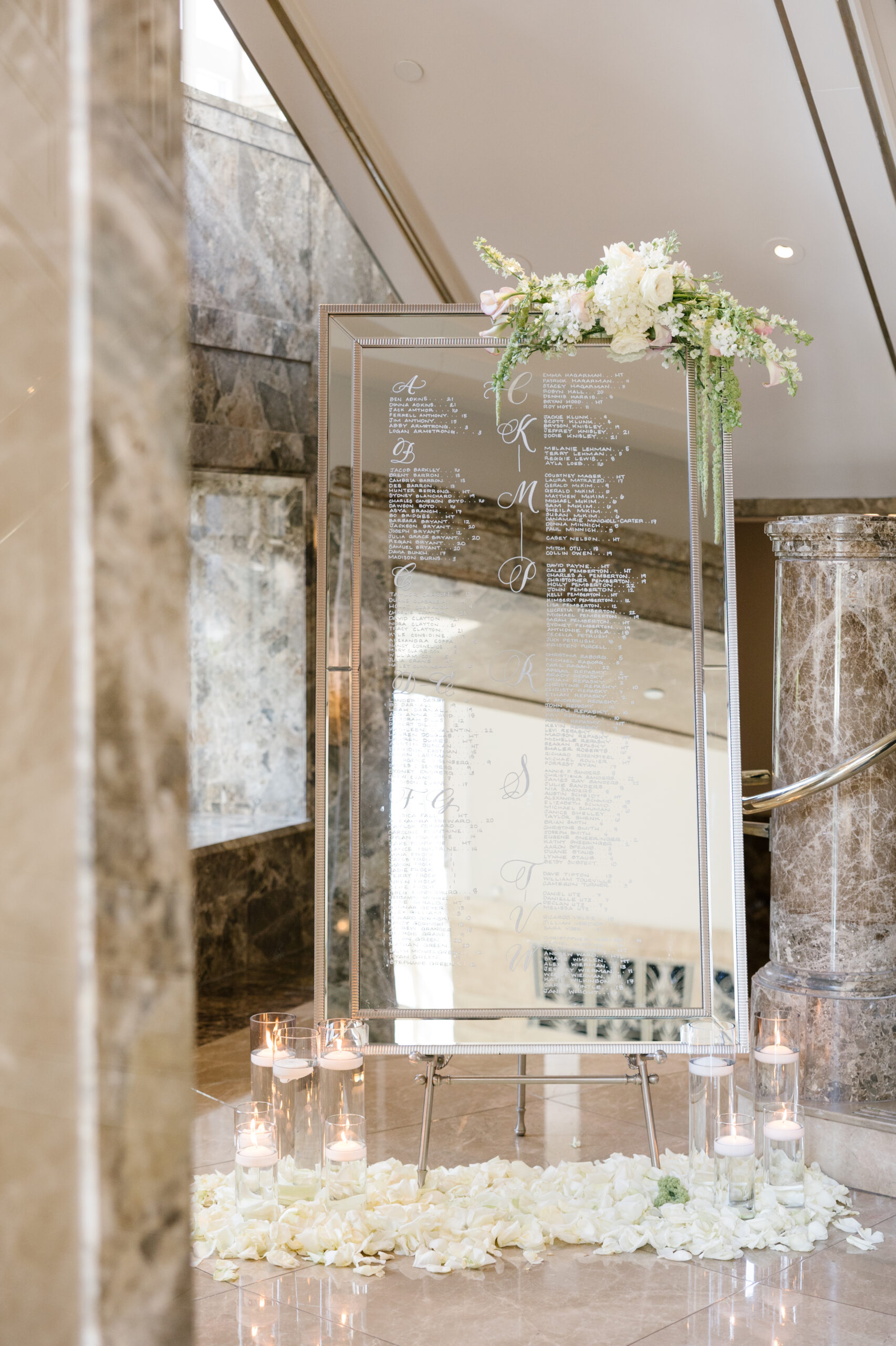 mirrored seating chart styled with florals at top corner and surrounded by glass vases with floating candles from Elevated Nashville Symphony Wedding reception.