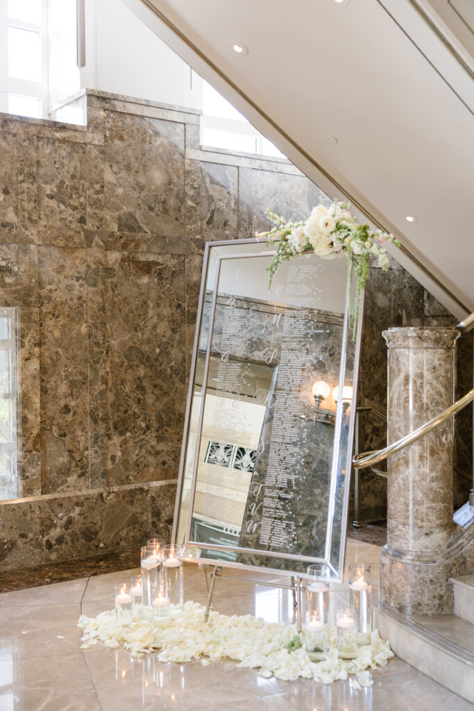 mirrored seating chart styled with florals at top corner and surrounded by glass vases with floating candles. 