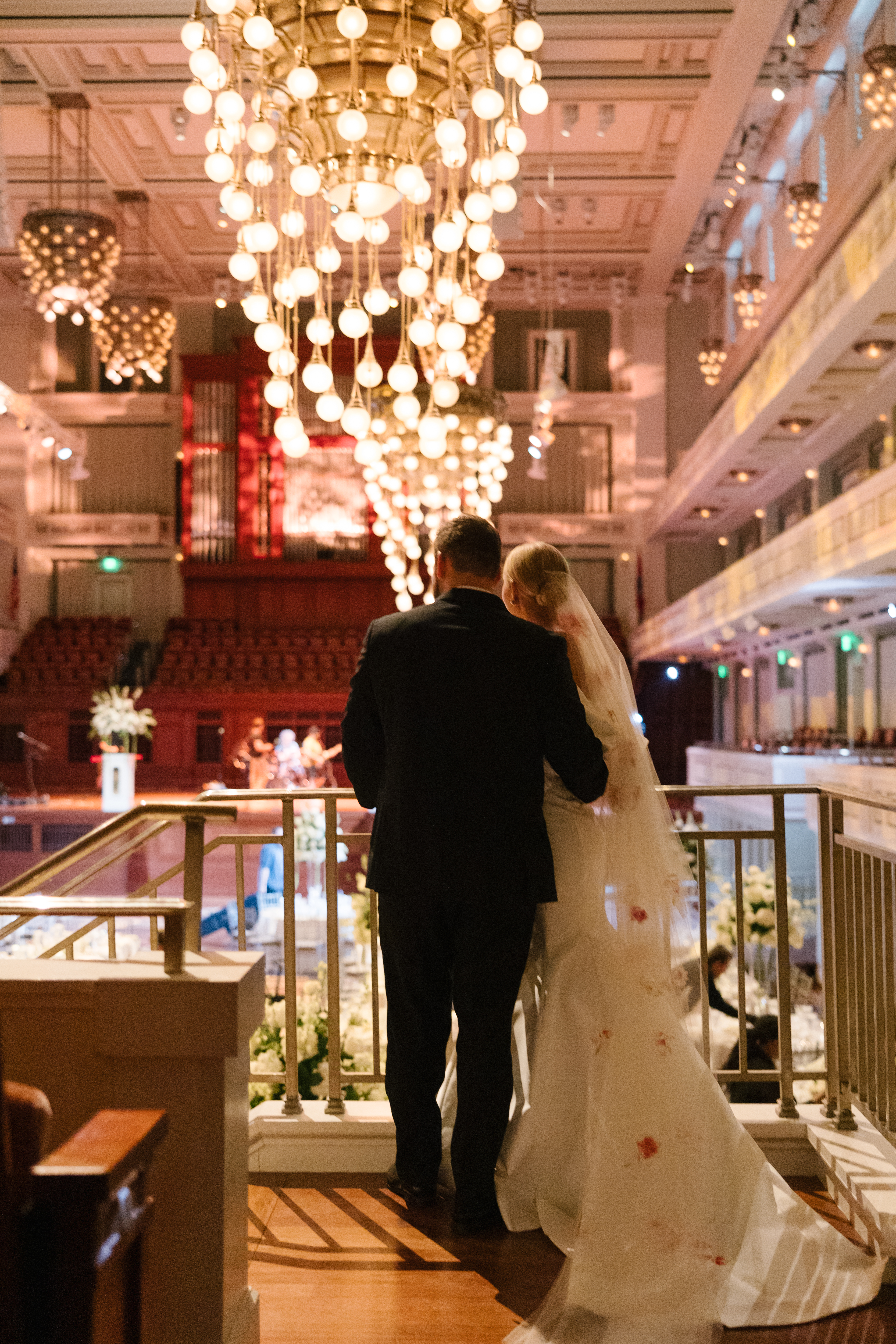 Bride and groom share an embrace as the look on at the reception space with chandelier above them. 