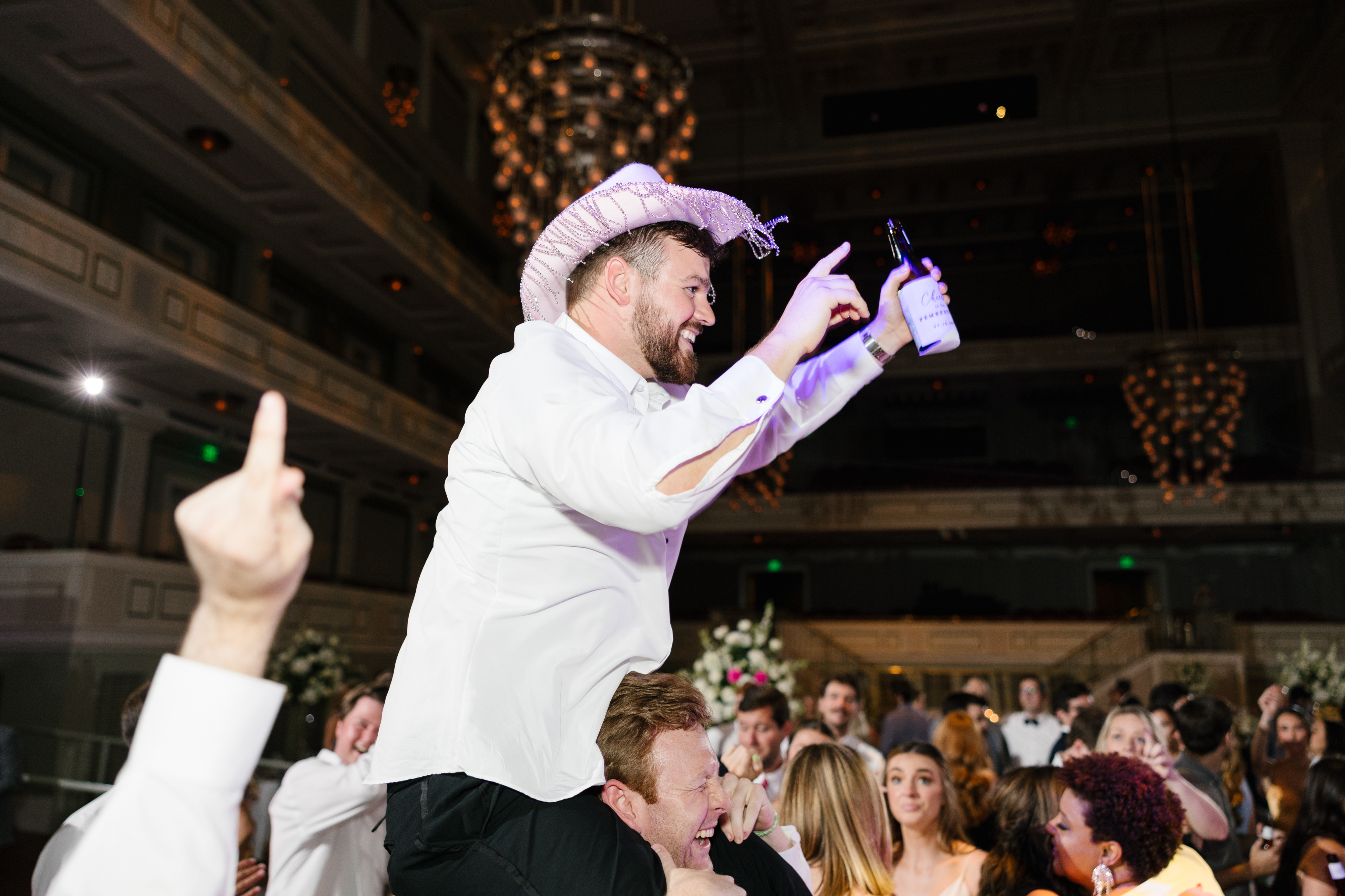 Groom on a person's shoulders. Wearing a cowboy hat on the dance floor at reception.