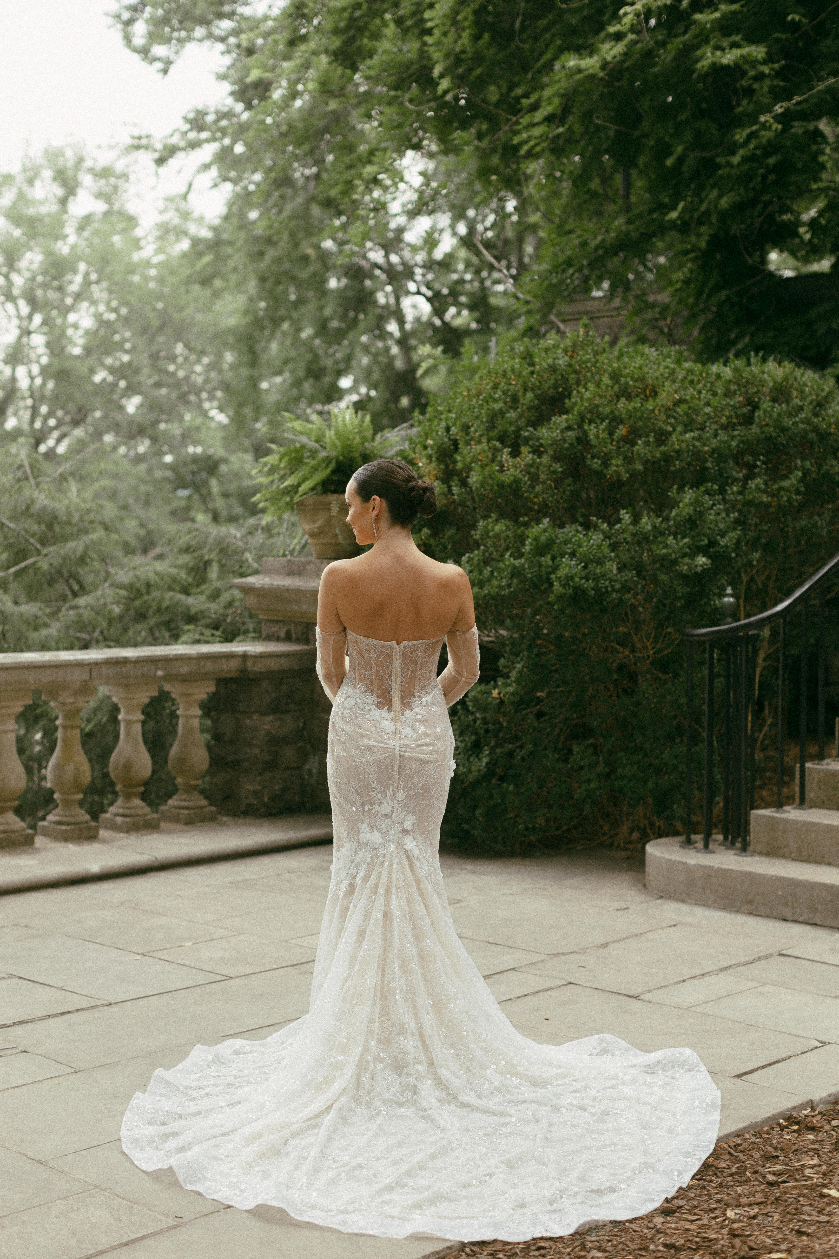 Bride on a terrace surrounded by greenery turned to show the back of her gown. 