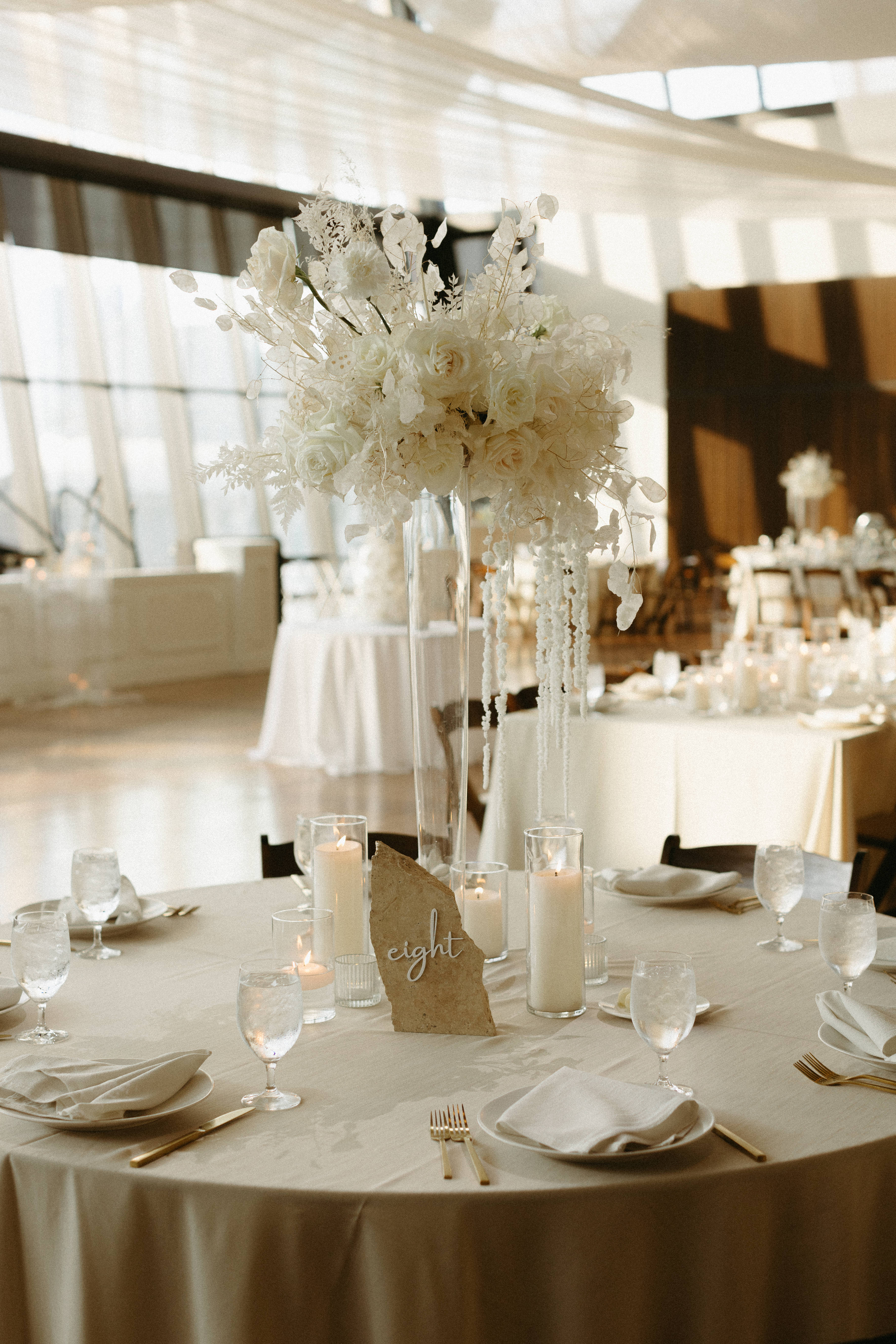 Stone table number atop formal tablescape with white florals and linen.