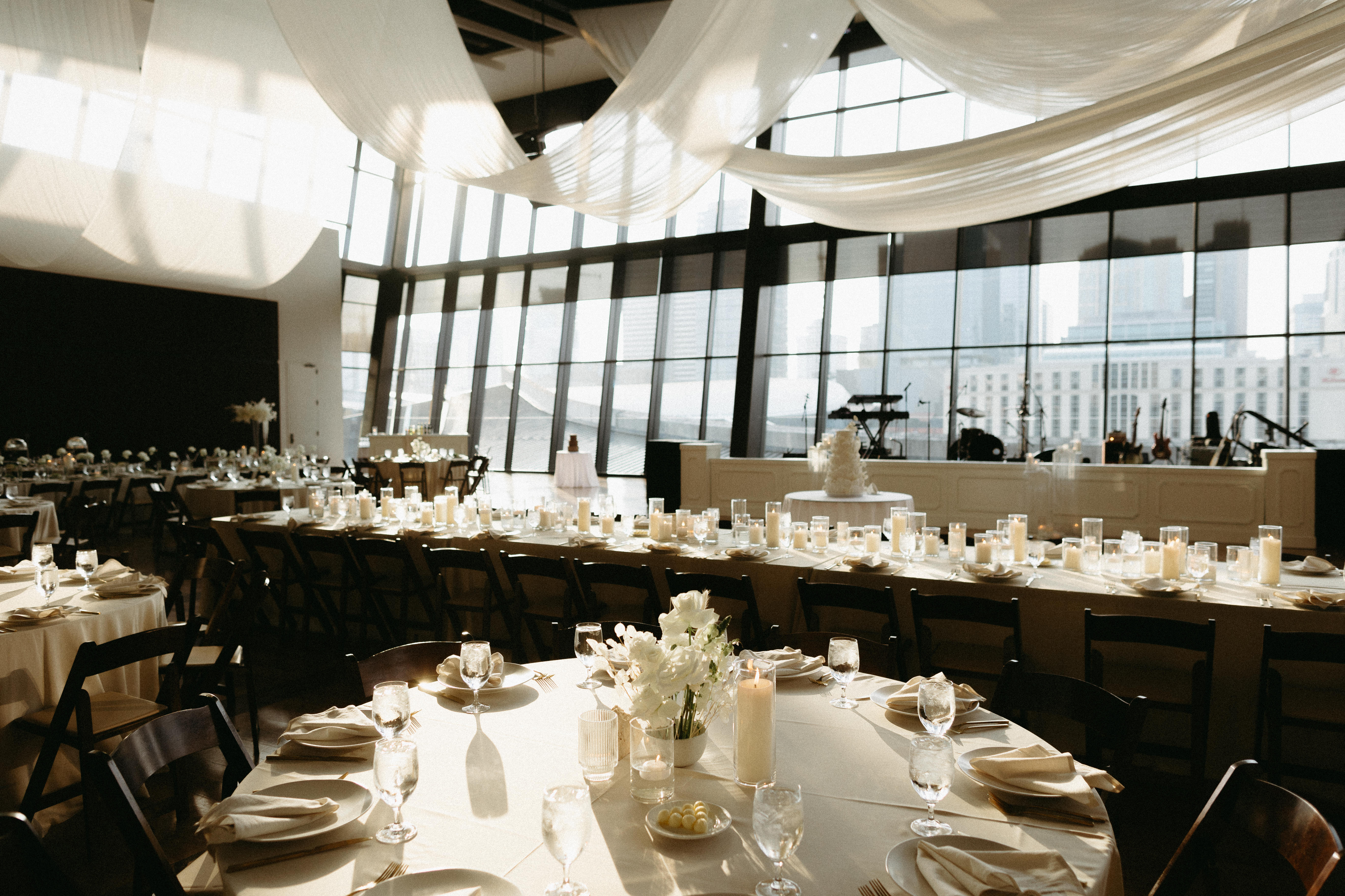 Formal dinning tables in a grand reception area with large windows and sunlight beaming down. 