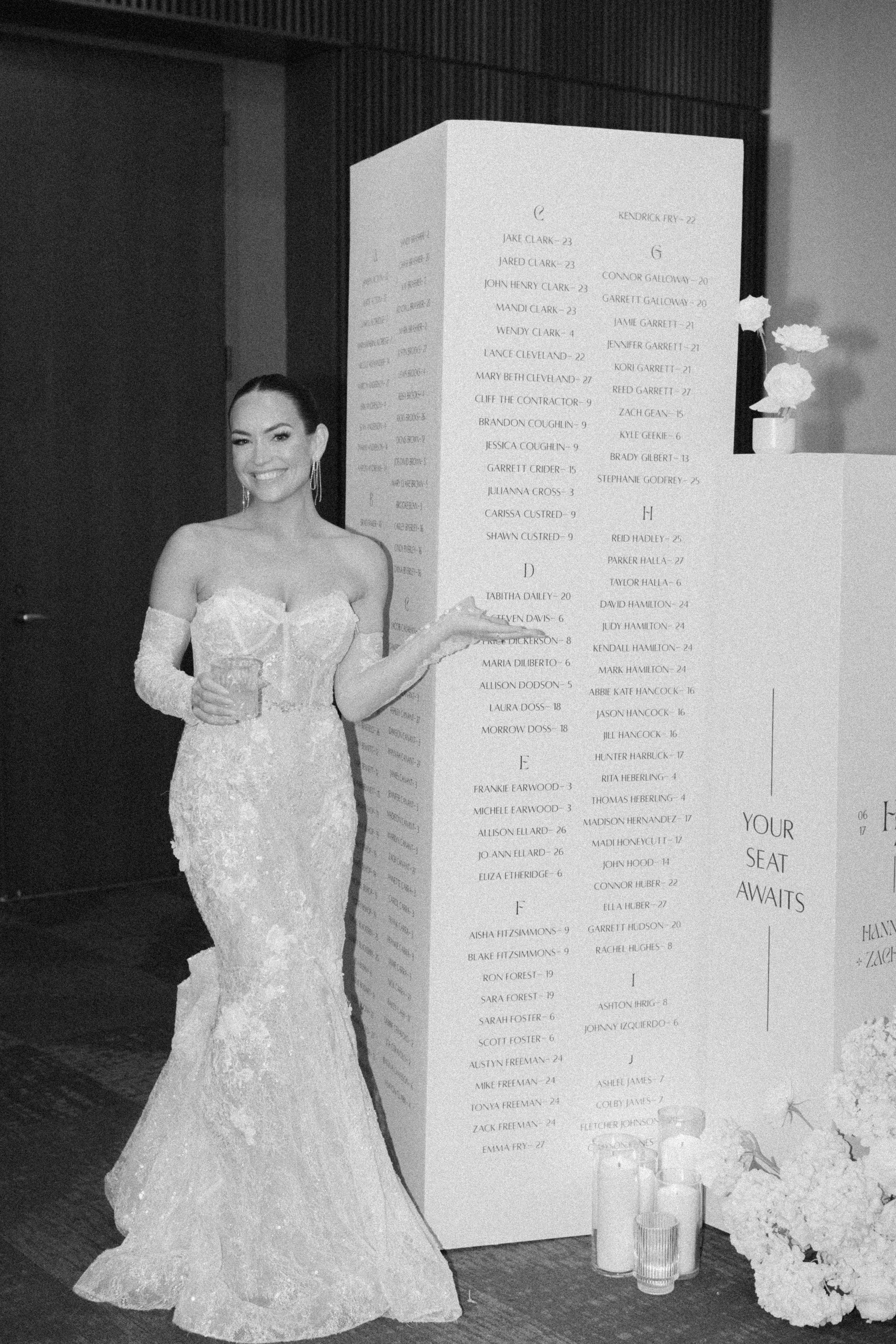 Bride standing beside white seating chart columns styled with white candles and white florals.