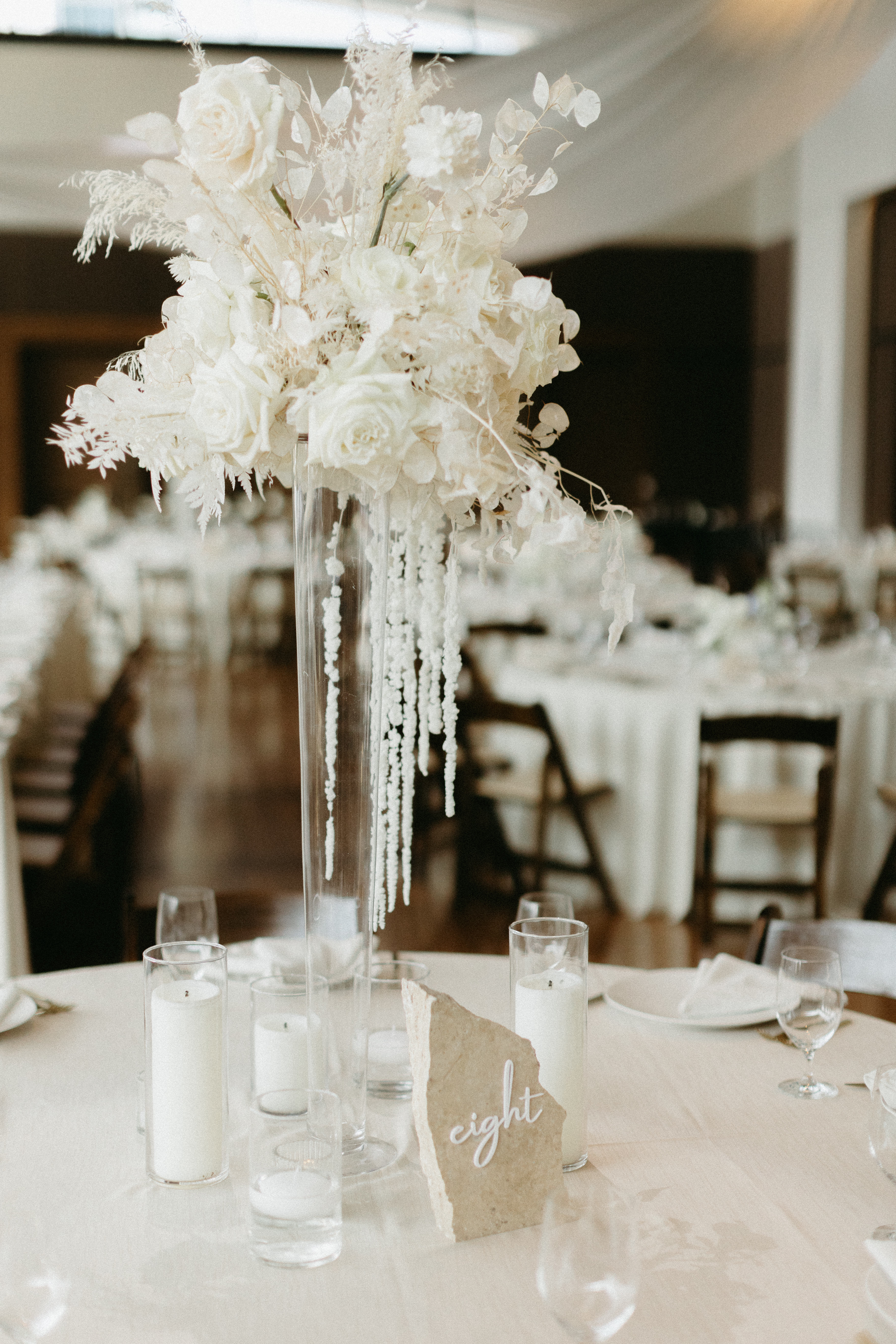 Stone table number atop formal tablescape with white florals and linen.