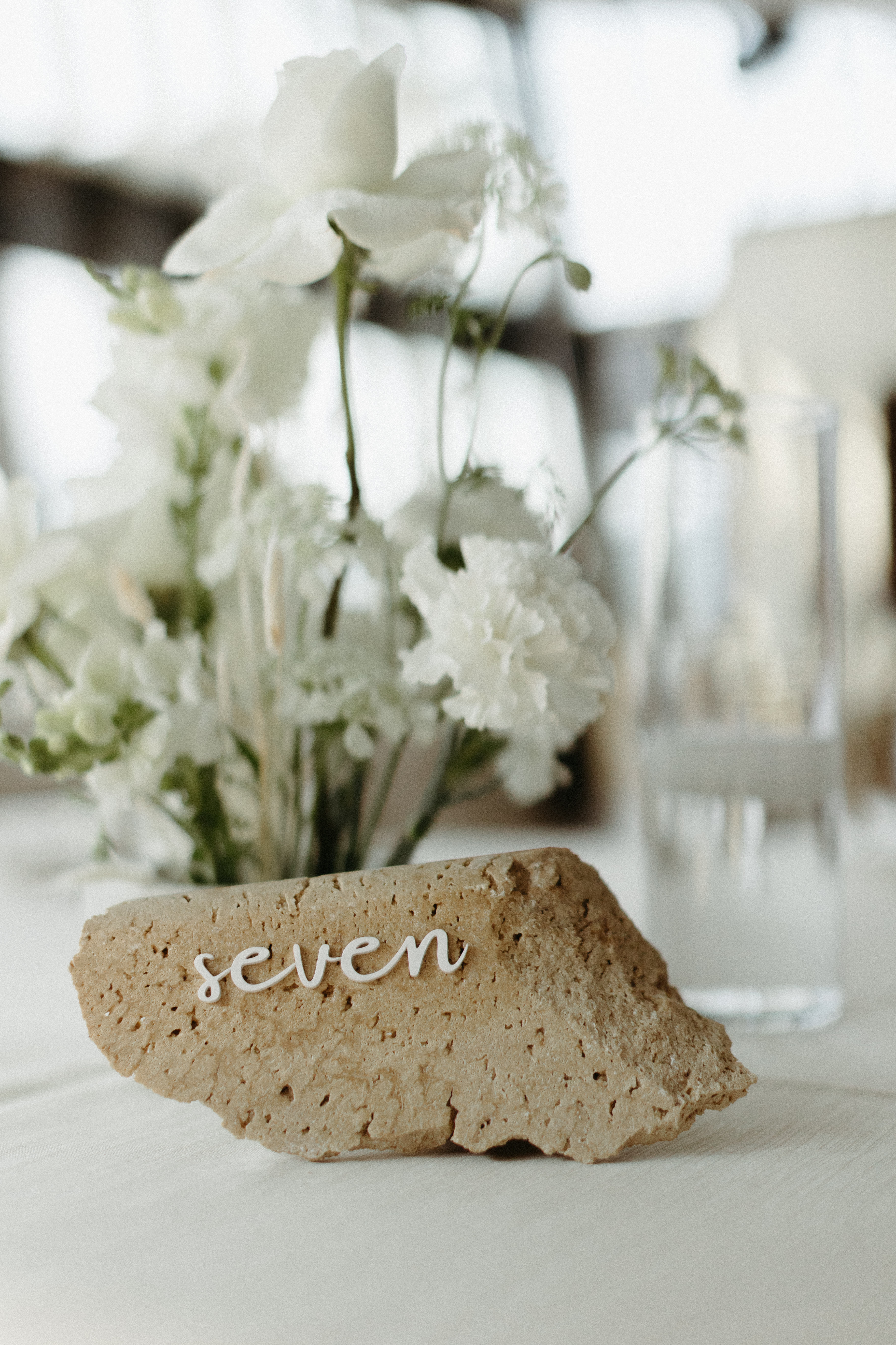 Stone table number atop formal tablescape with white florals and lined. 