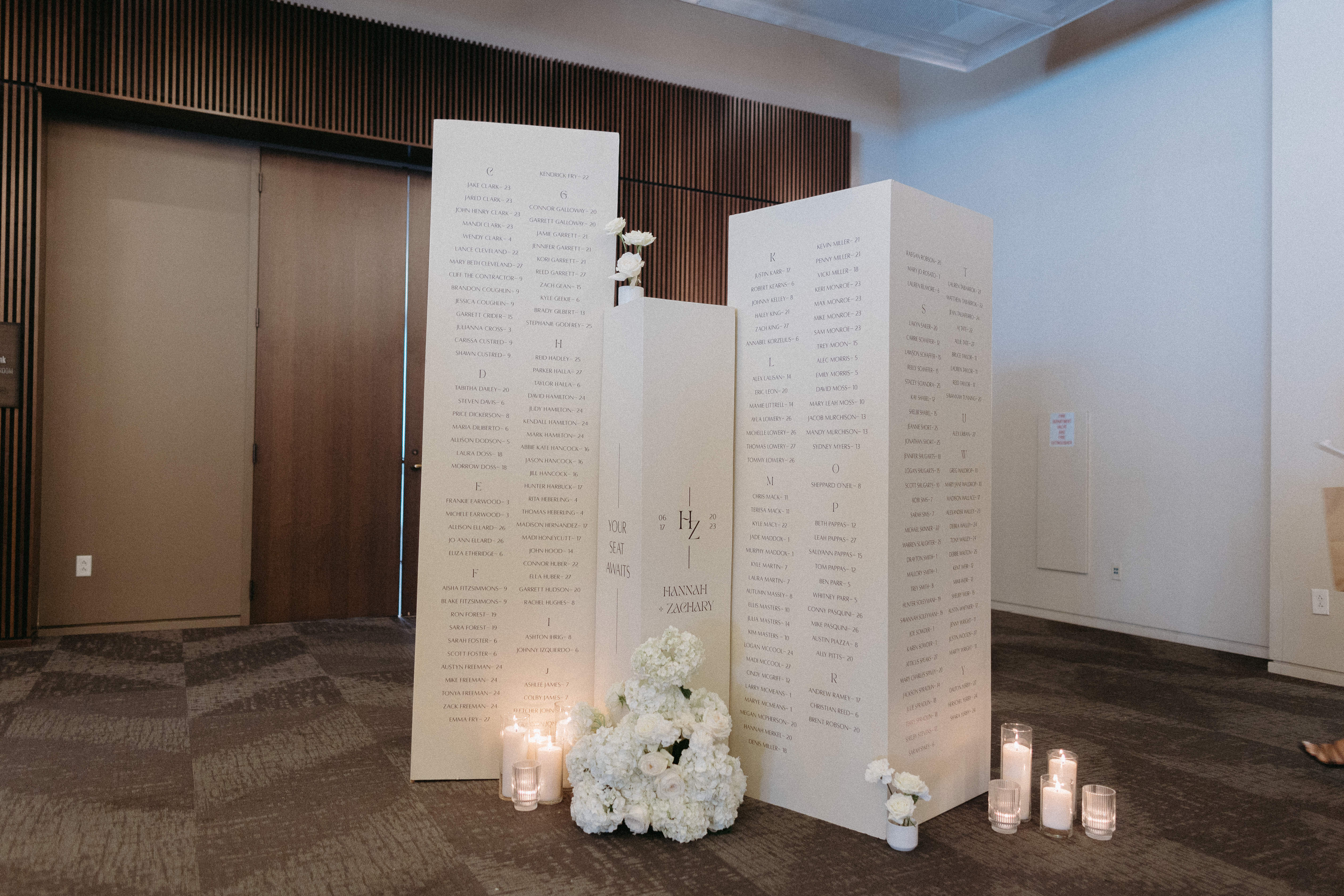 White seating chart columns styled with white candles and white florals.