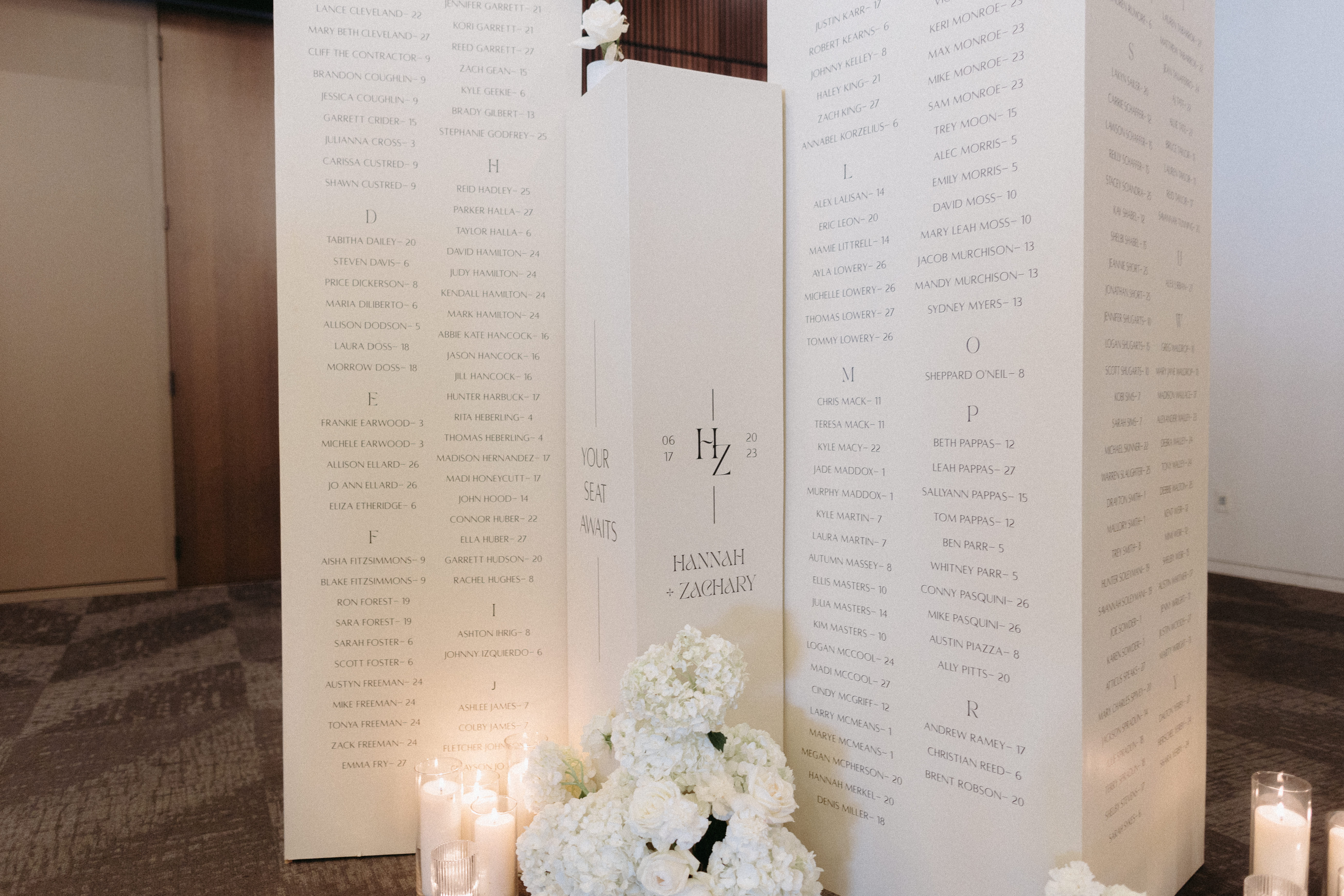 White seating chart columns styled with white candles and white florals.