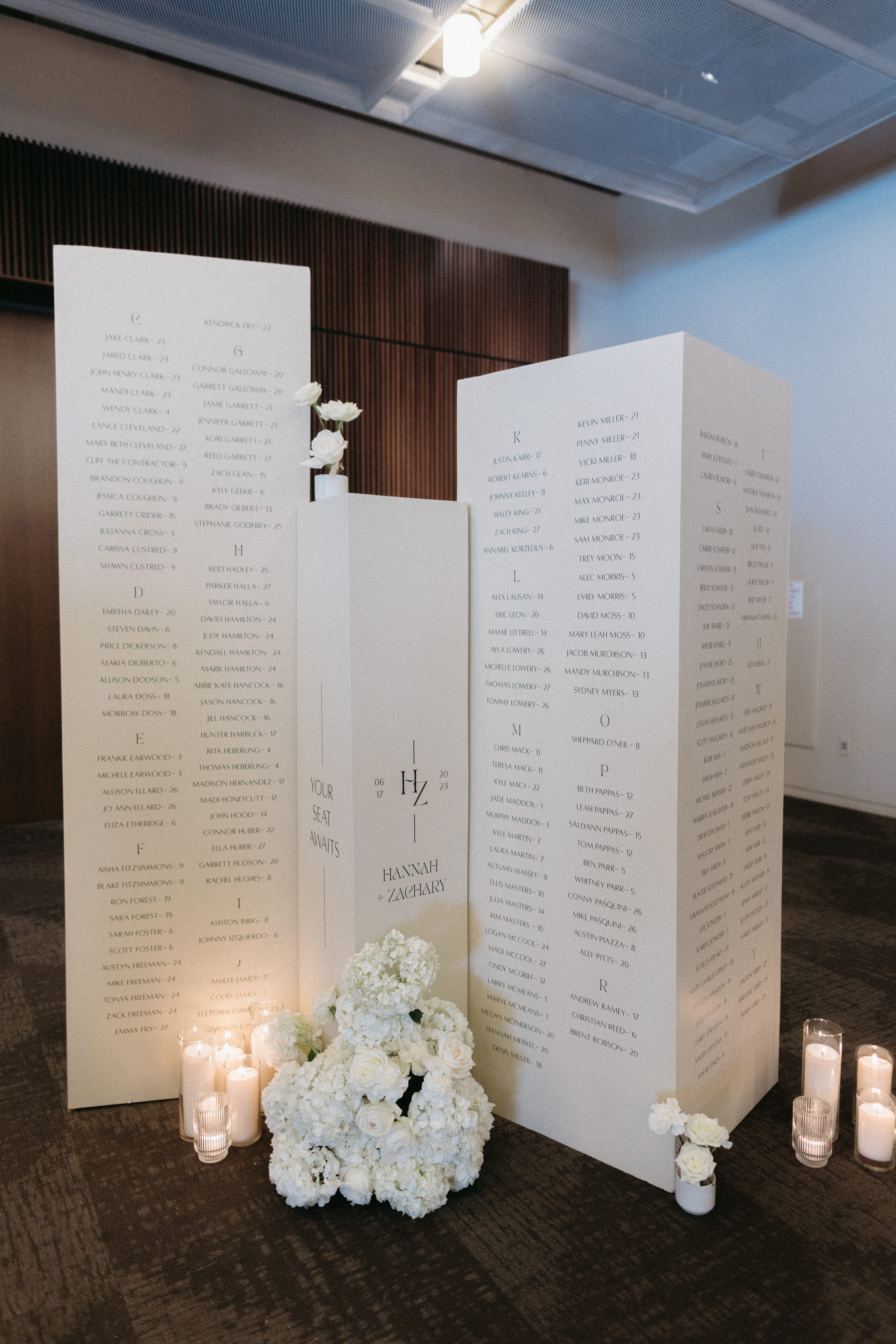 White seating chart columns styled with white candles and white florals.