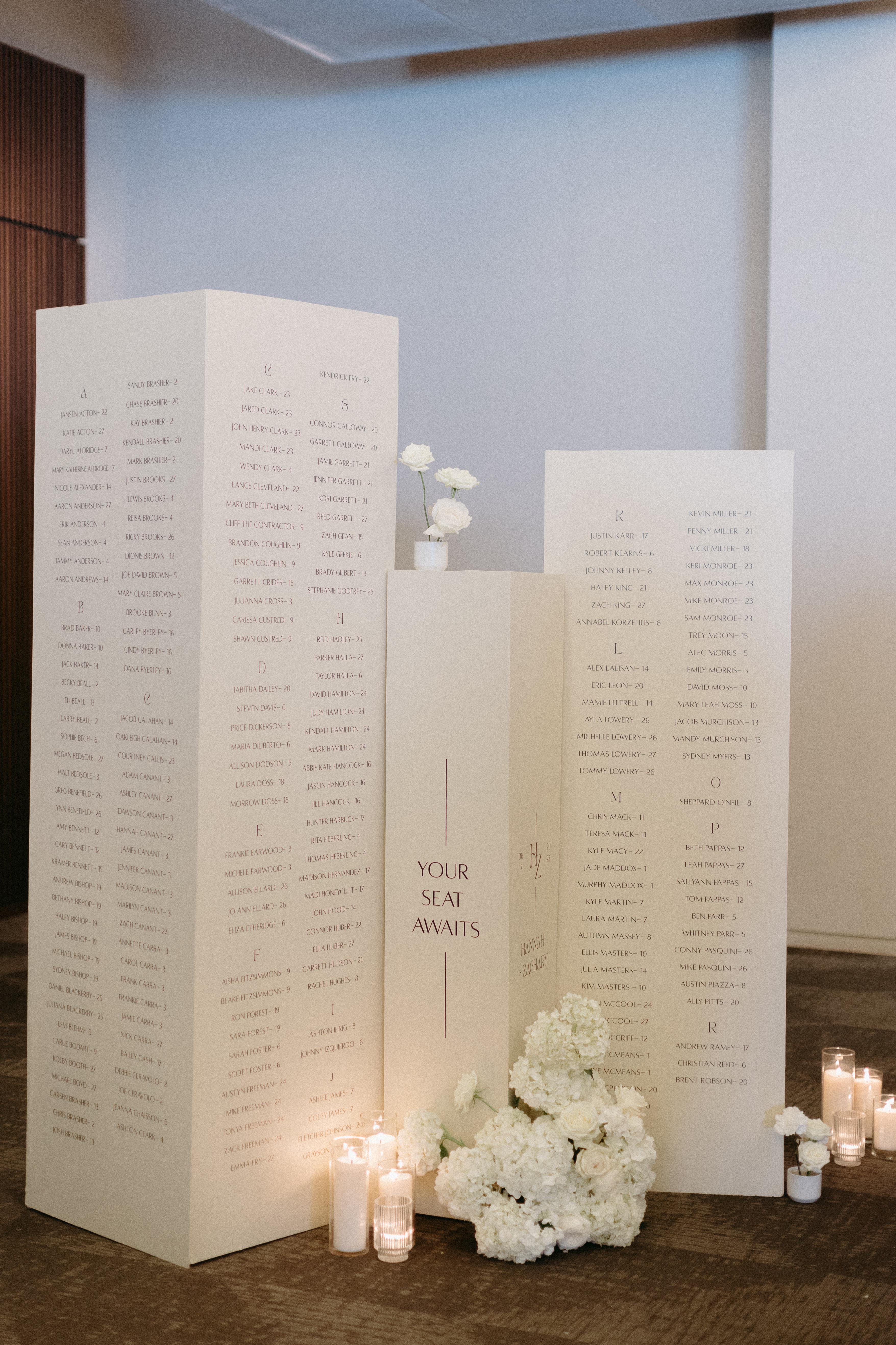 White seating chart columns styled with white candles and white florals.