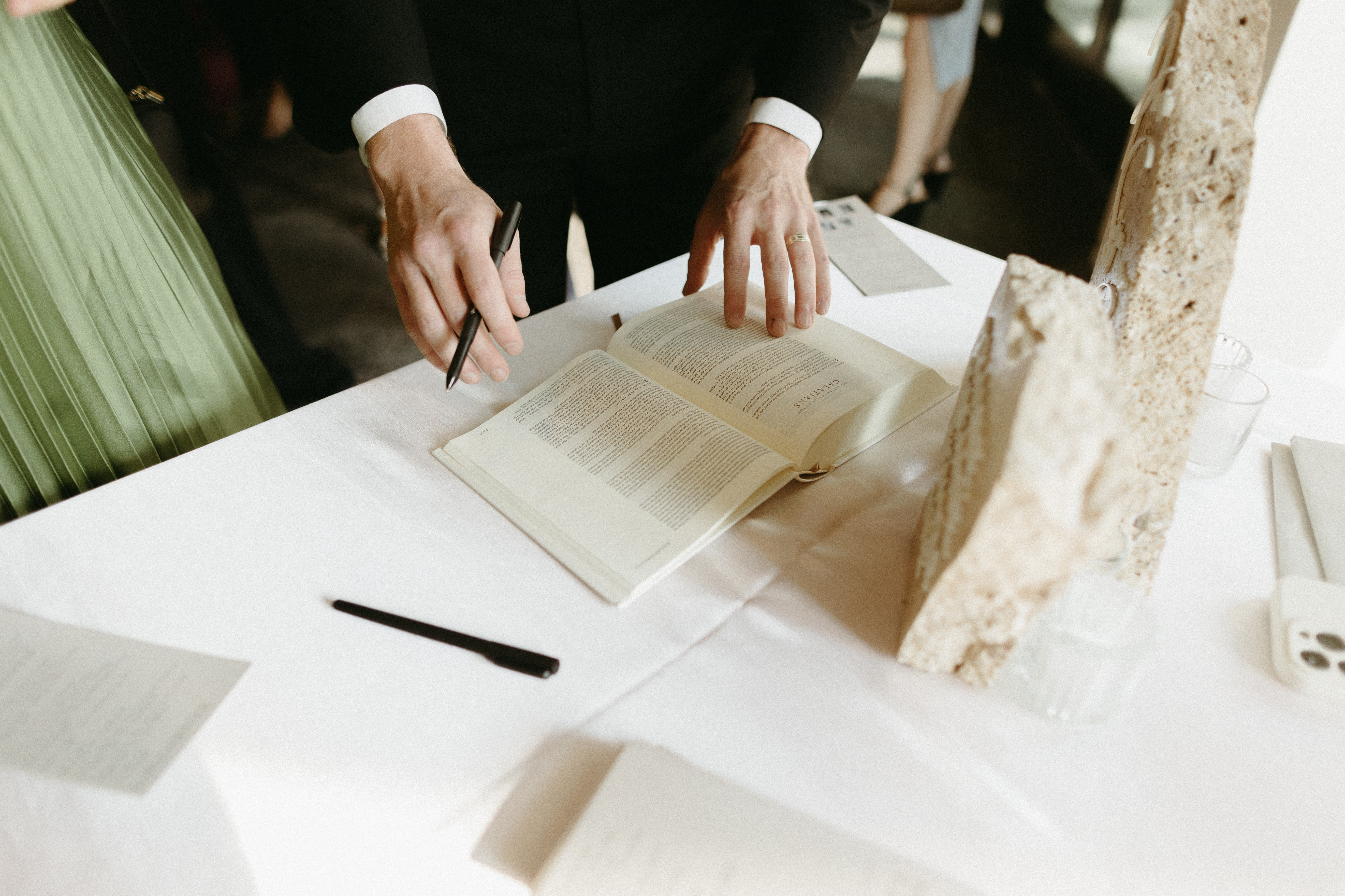 Stones and a Bible sitting on top of a table in front of a window as a hand holds the side of the Bible.