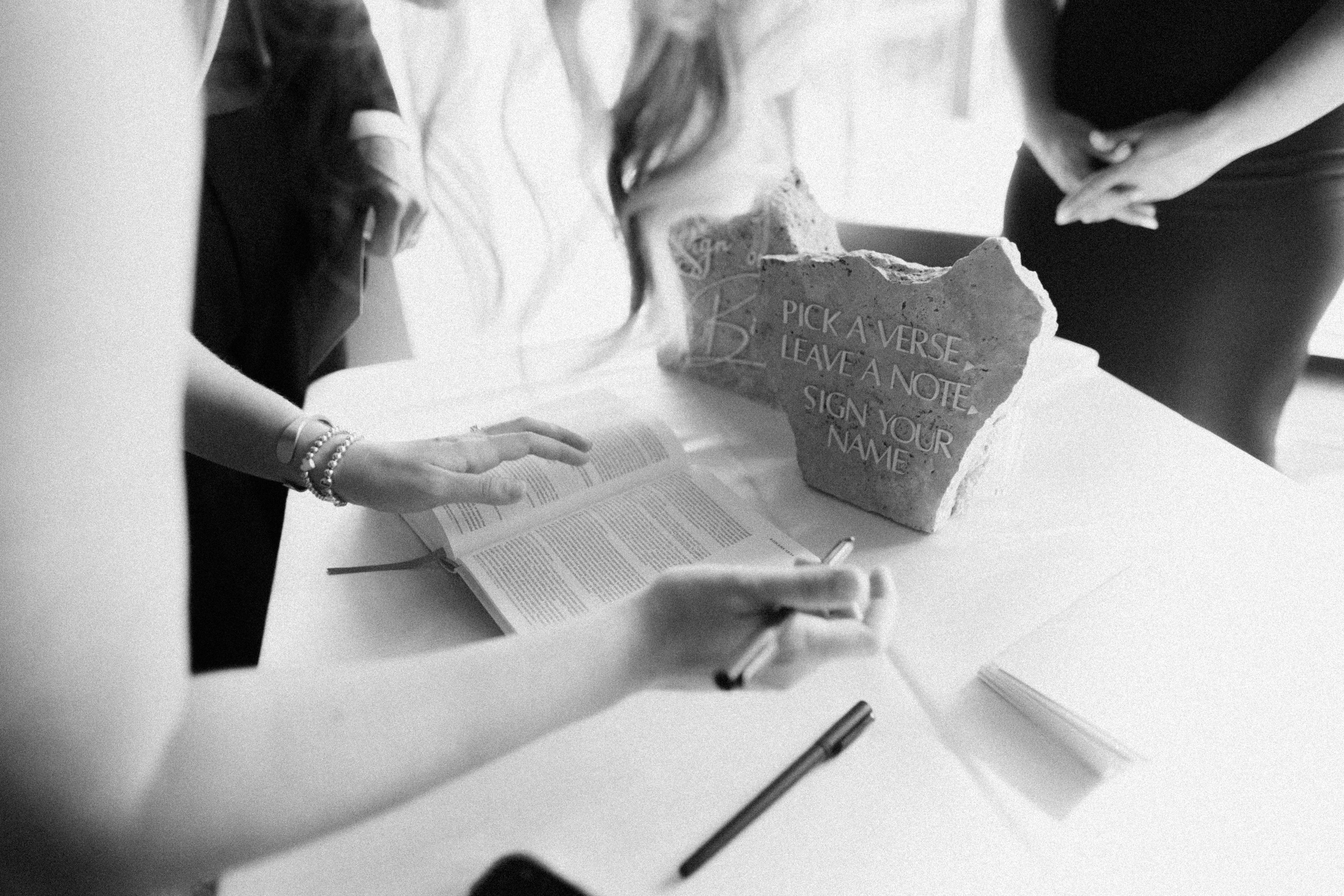 Stones and a Bible sitting on top of a table in front of a window as a hand holds the side of the Bible.