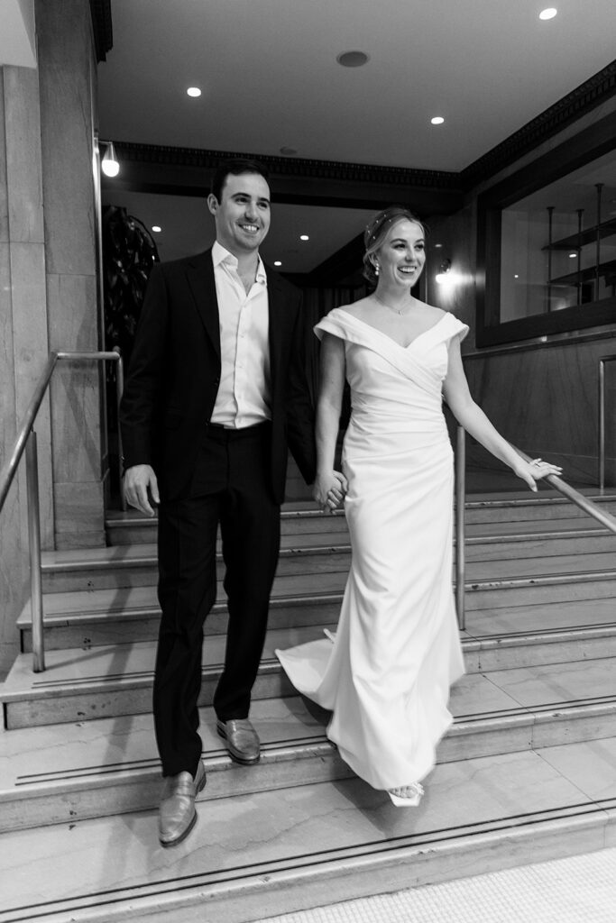 Bride and groom smiling and walking down stairs together.