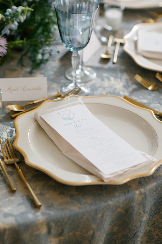 Formal place setting including gold rimmed plate topped with napkin and custom dinner menu.
