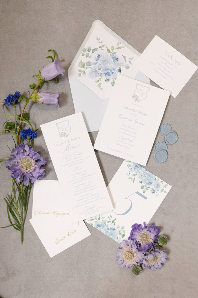 Custom Rehearsal invitation suite, menu, and table number styled with purple florals to match.