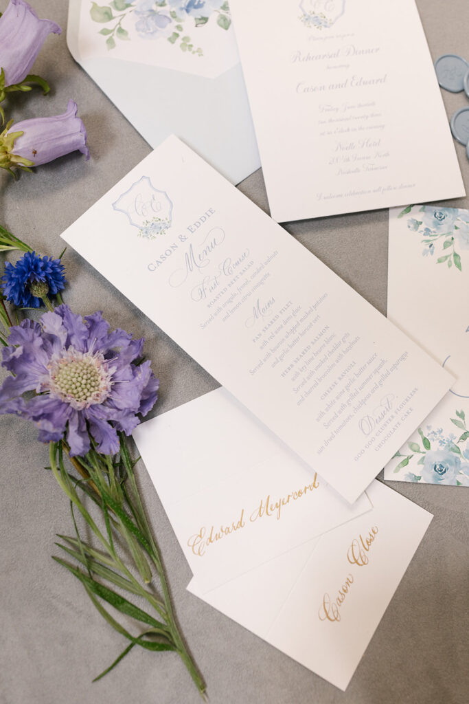 Custom Rehearsal invitation suite, menu, and table number styled with purple florals to match.