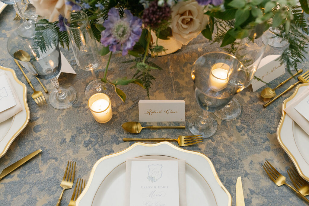 Formal place setting including gold rimmed plate topped with napkin and custom dinner menu.