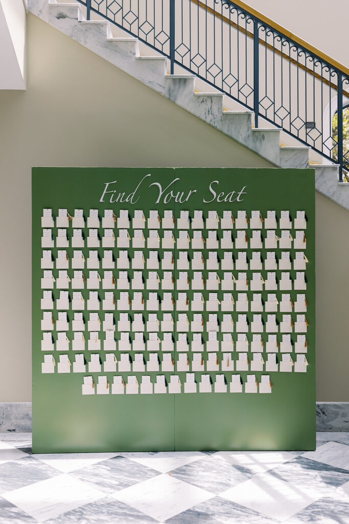 Green seating chart display standing on black and white checkered floor, boasting custom bookmark escort cards.
