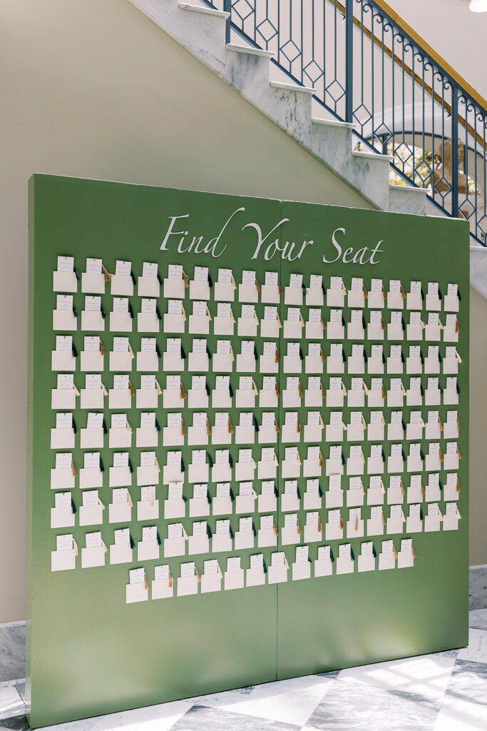 Green seating chart display standing on black and white checkered floor, boasting custom bookmark escort cards.