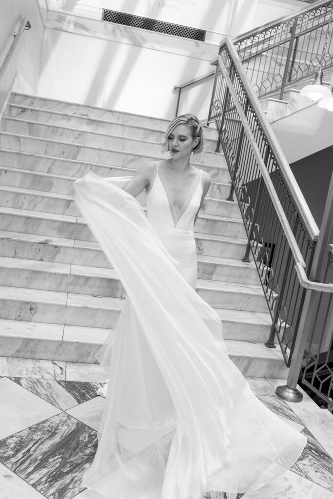 Bride standing on stairs waiving train on gown to the side of her.