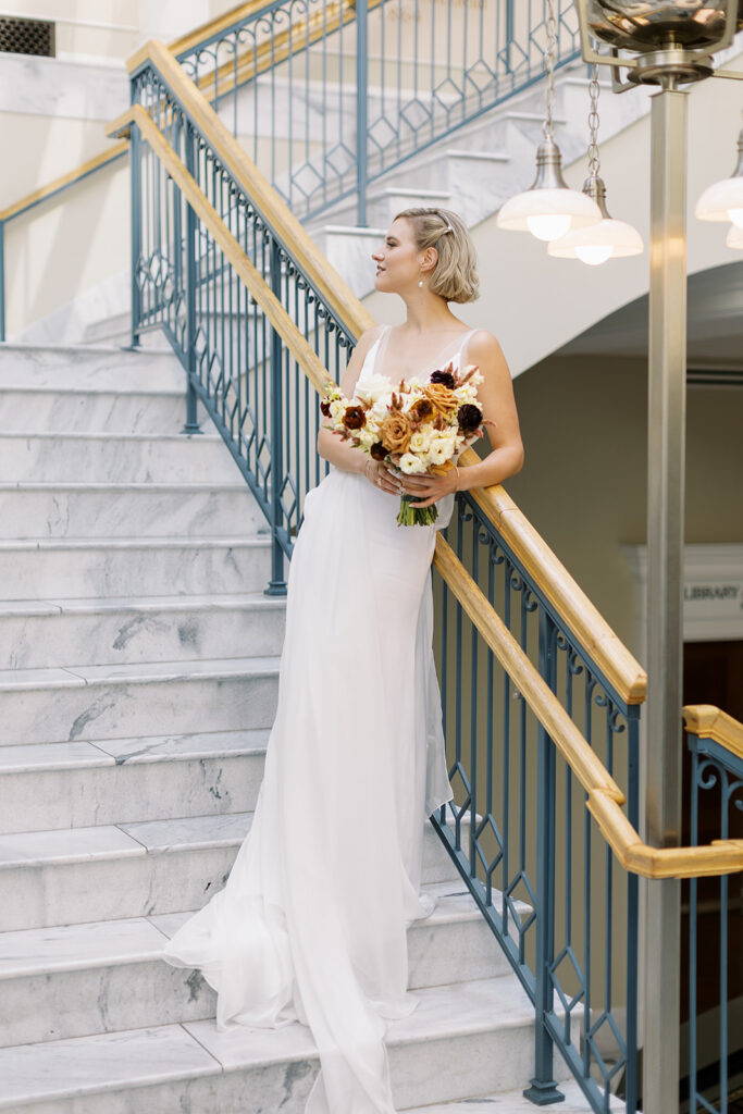 Bride standing on stairs holding bouquet looking to the side.