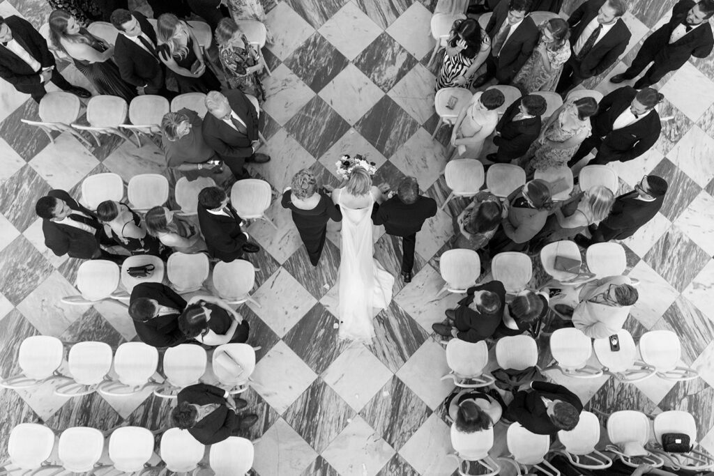Aerial view of bride and groom walking down the black and white checkered aisle. 