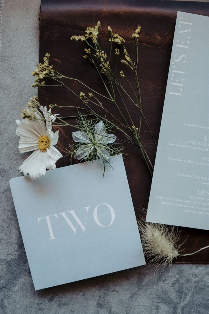 Flat lay of reception menu and table number styled with wild flowers.