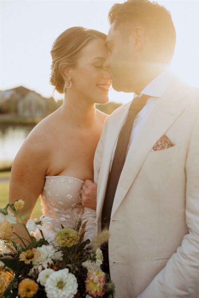 Bride leaning into groom with eyes closed as the sun sets behind them.