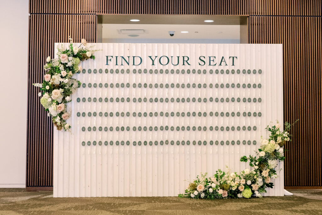 Seating chart wall displaying oval, tasseled escort cards. Styled with florals.