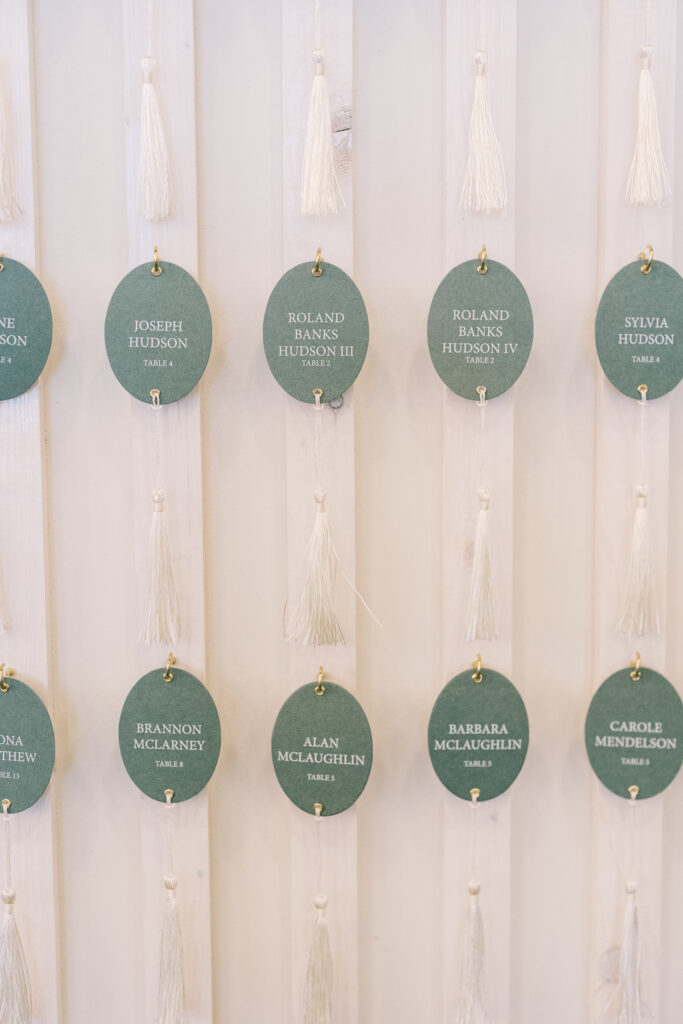 Seating chart wall displaying oval, tasseled escort cards.