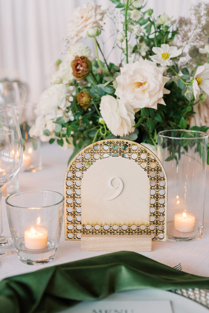 Wooden, laser-cut table number sign on table with candles and florals.