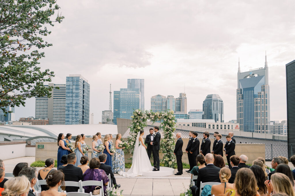 Wedding party and guests at outdoor ceremony venue with Nashville skyline in the background.