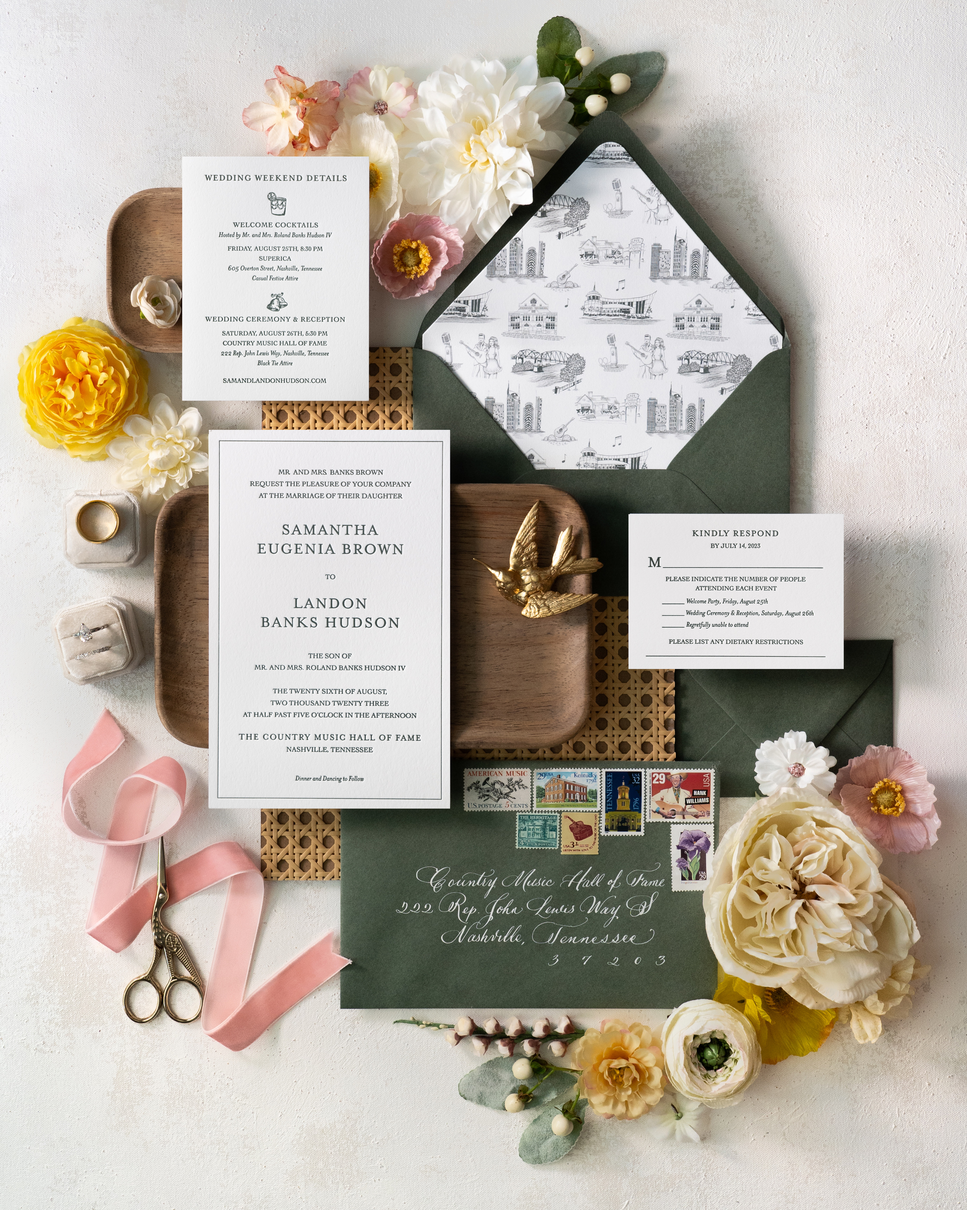 Custom wedding invitation suite flat lay styled with florals, wooden trays, ornamented pieces.