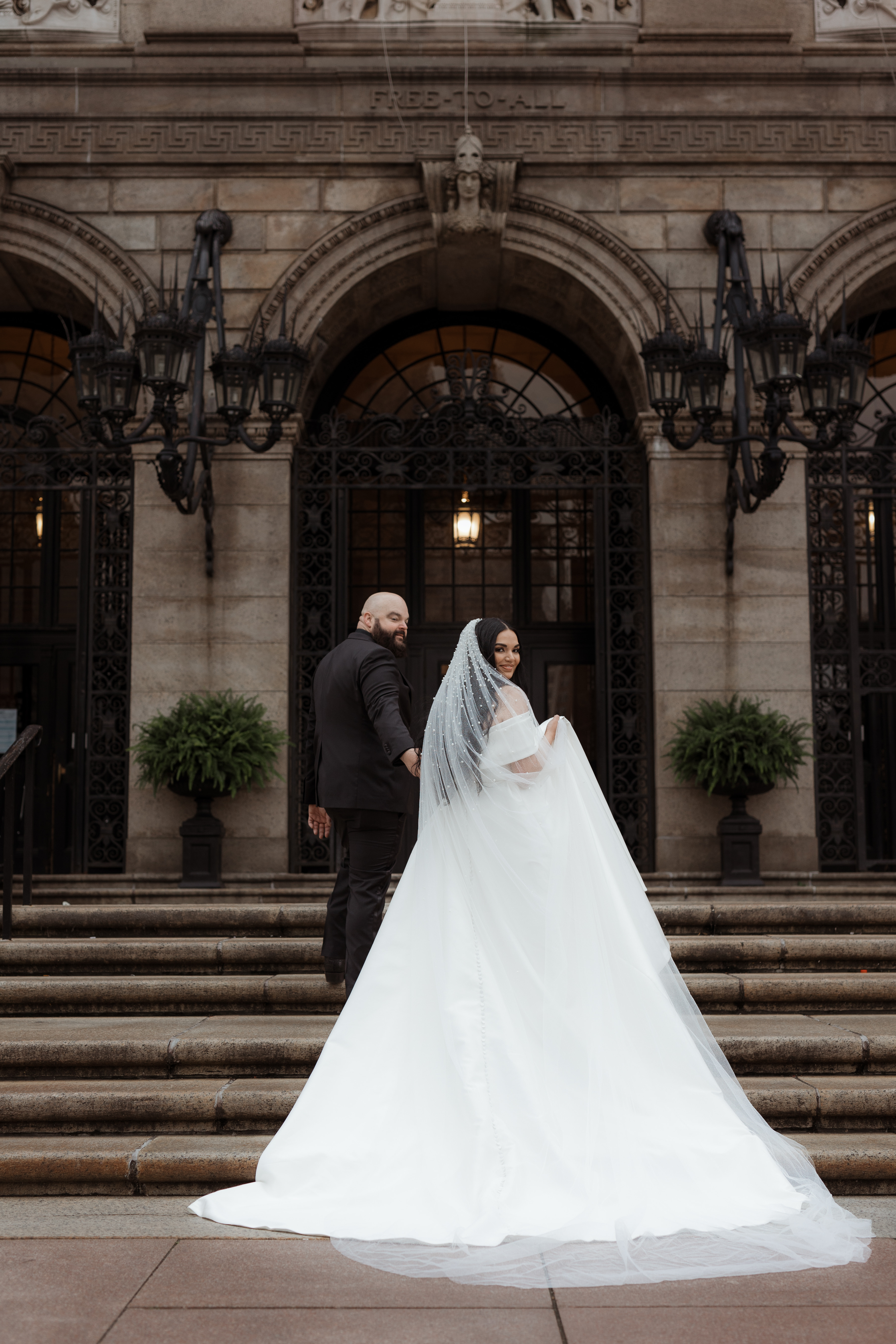Bride and groom walking up stairs towards entrance of Boston Public Library