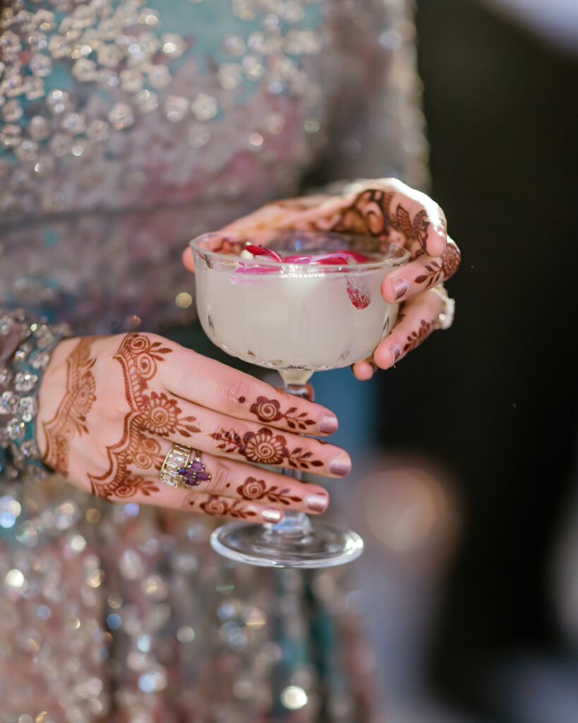 A woman's hands in Mendhi holding a drink.