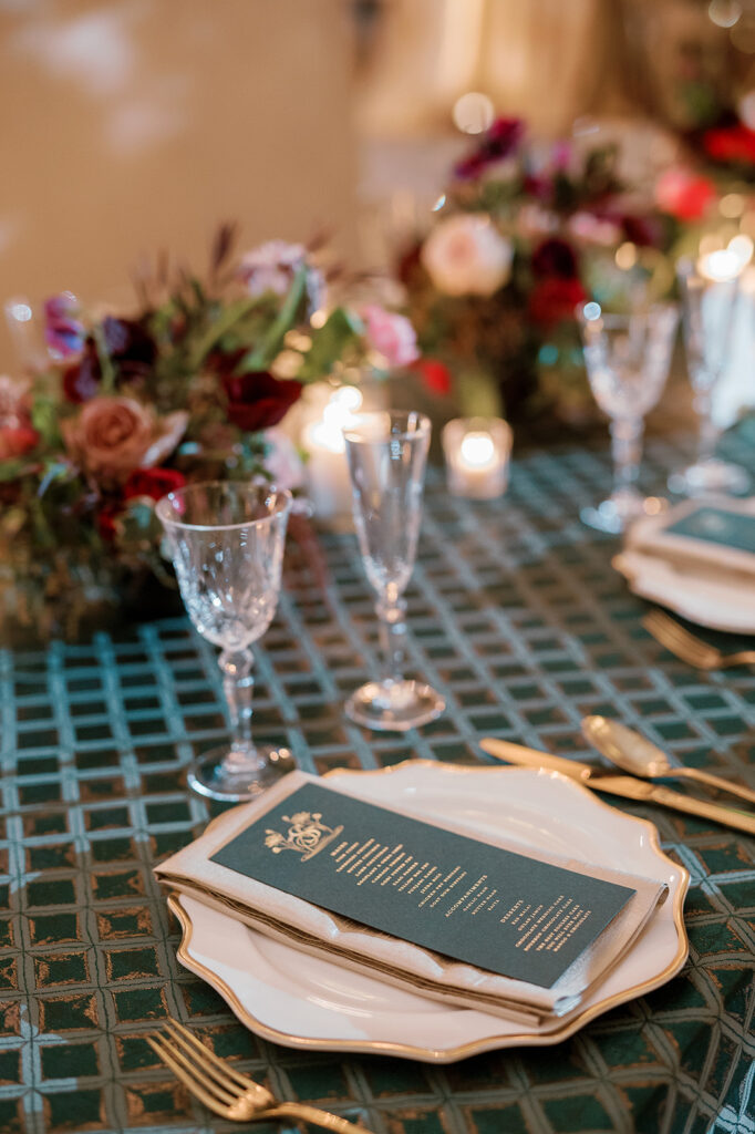 a formal dining setting including gold-rimed plating, goldware, florals, custom menu.