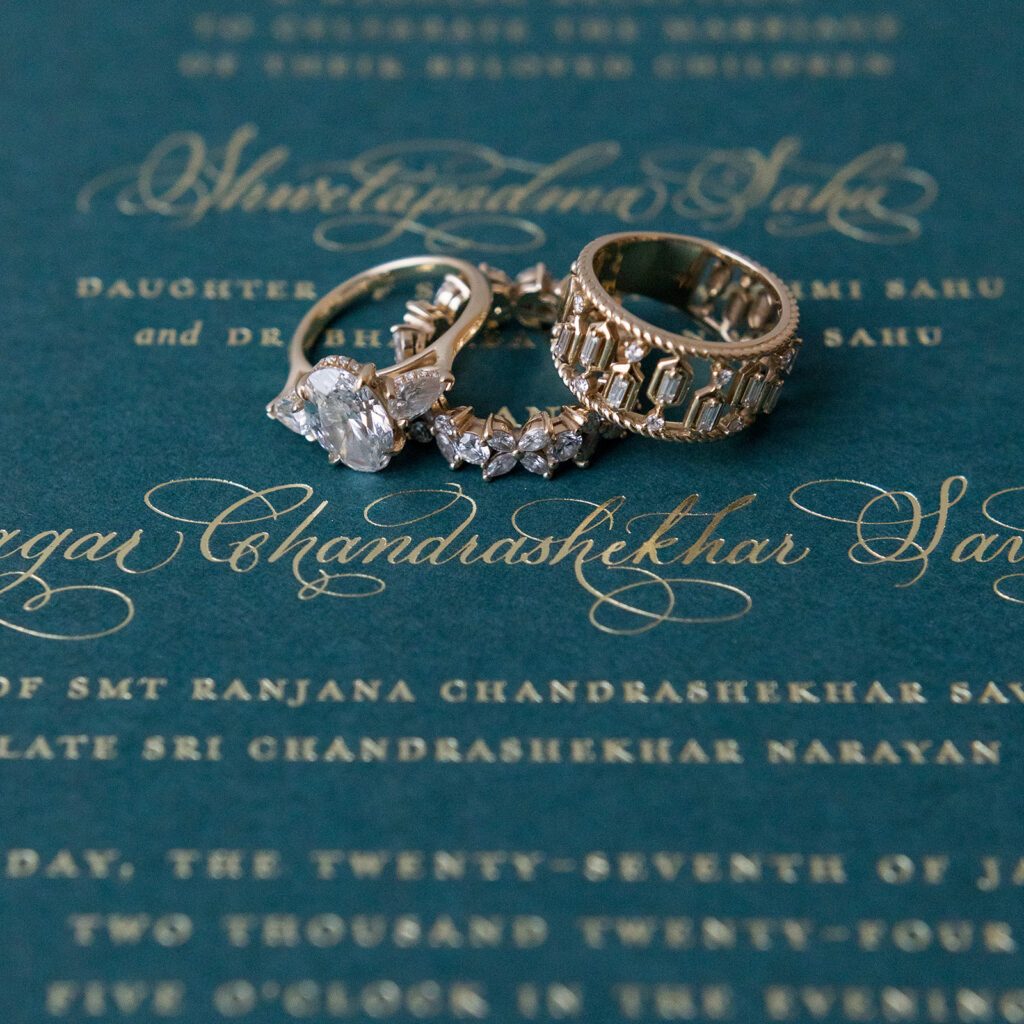 wedding rings sitting atop a custom invitation with gold lettering and caligraphy.